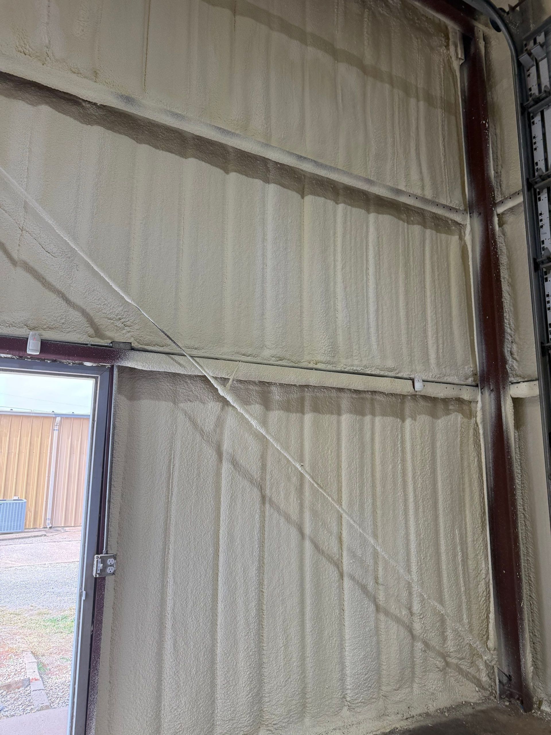 Interior wall insulated with light tan spray foam. Steel beams visible, with a doorway and window.