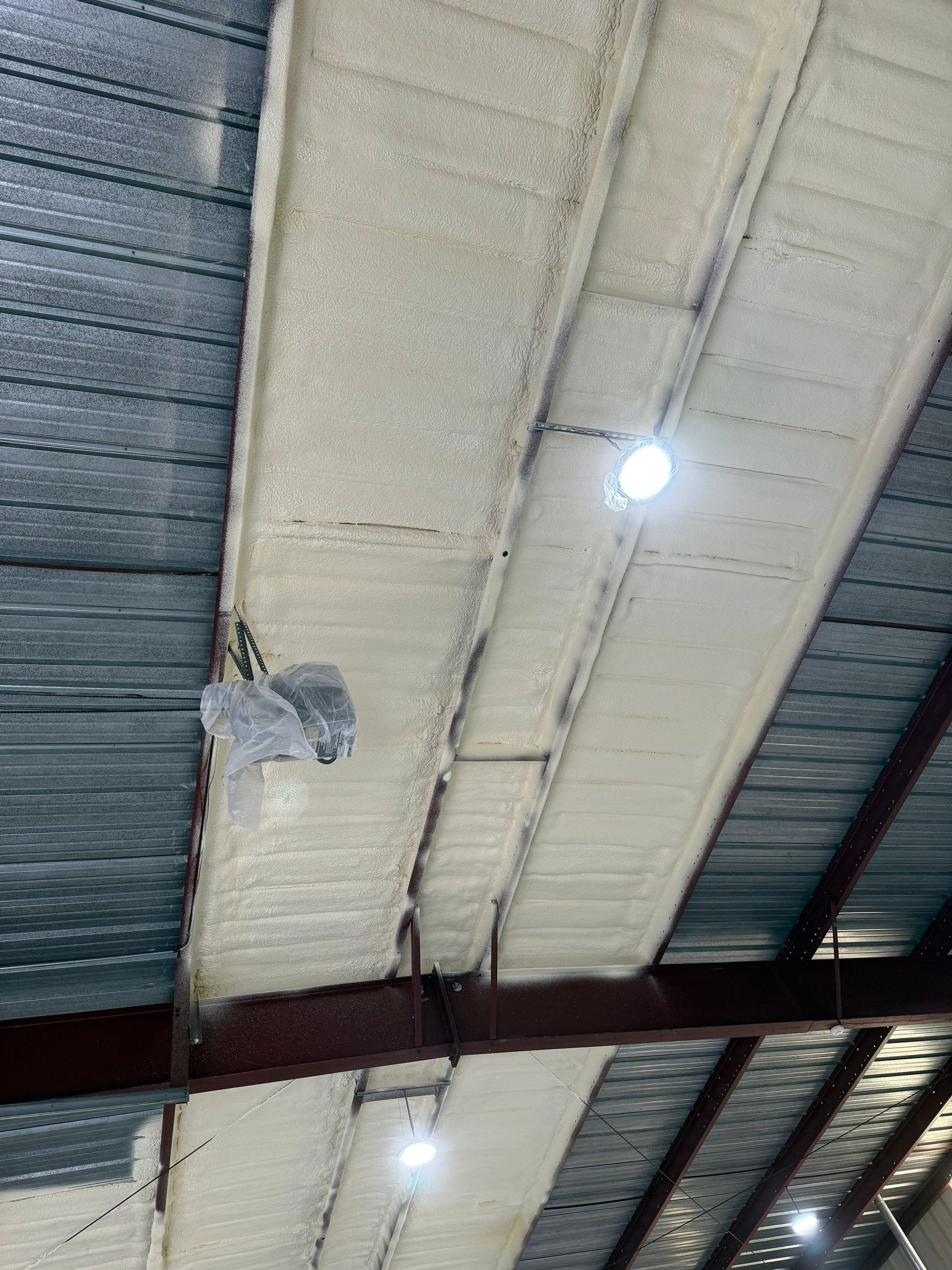 Arched ceiling with spray foam insulation, metal beams, and recessed lights.
