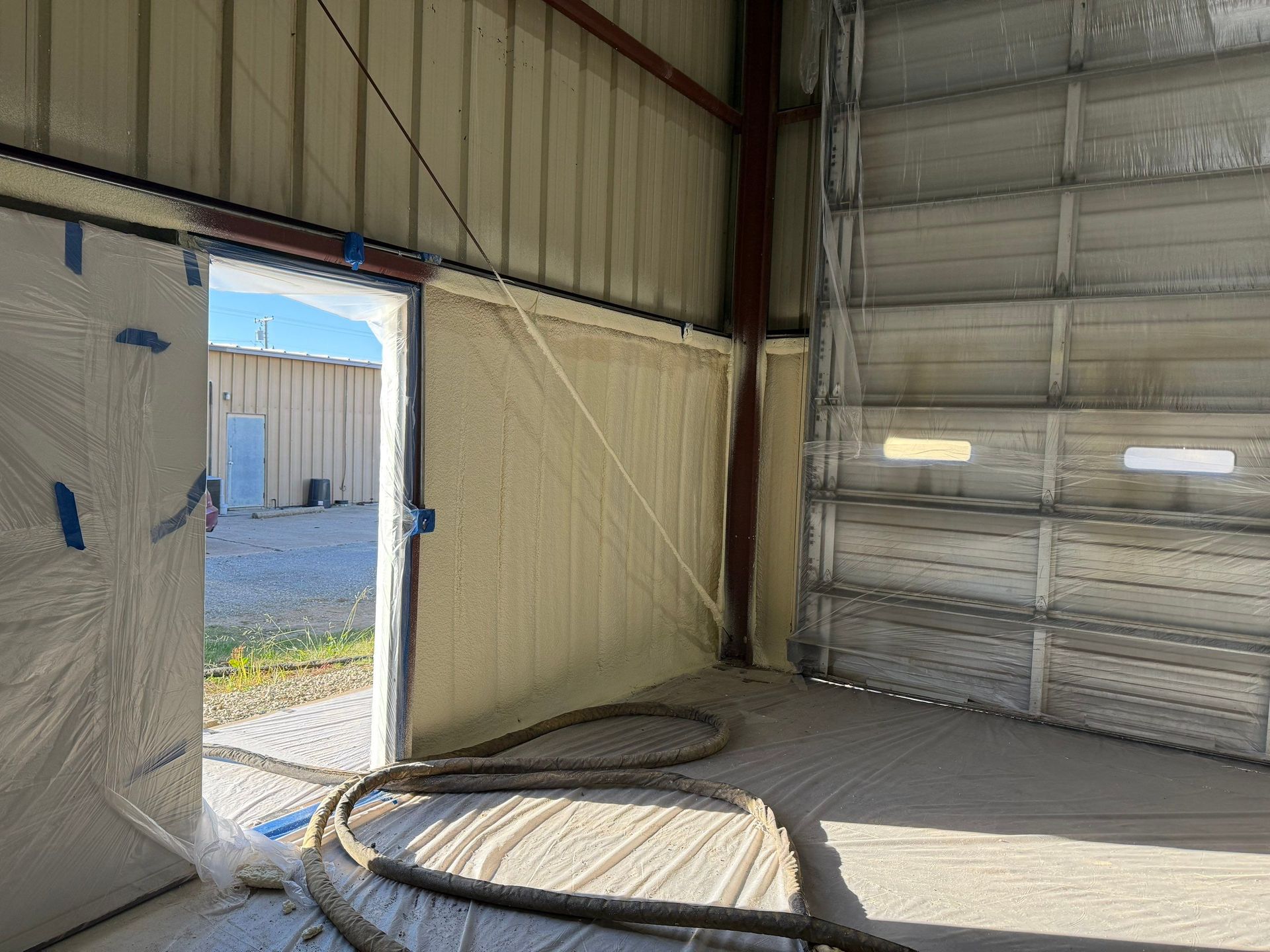 Spray foam insulation applied around an open doorway and garage door inside a metal building.