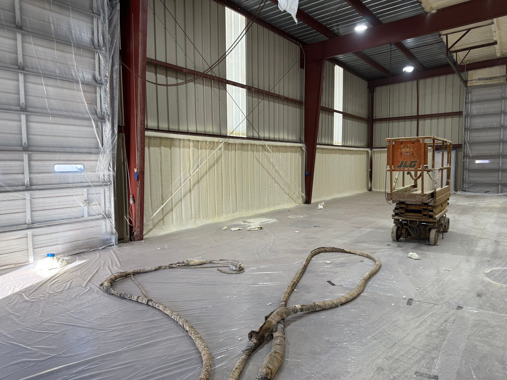 Interior of a warehouse with spray foam insulation on the walls. A lift is in the distance, and ropes lay on the floor.
