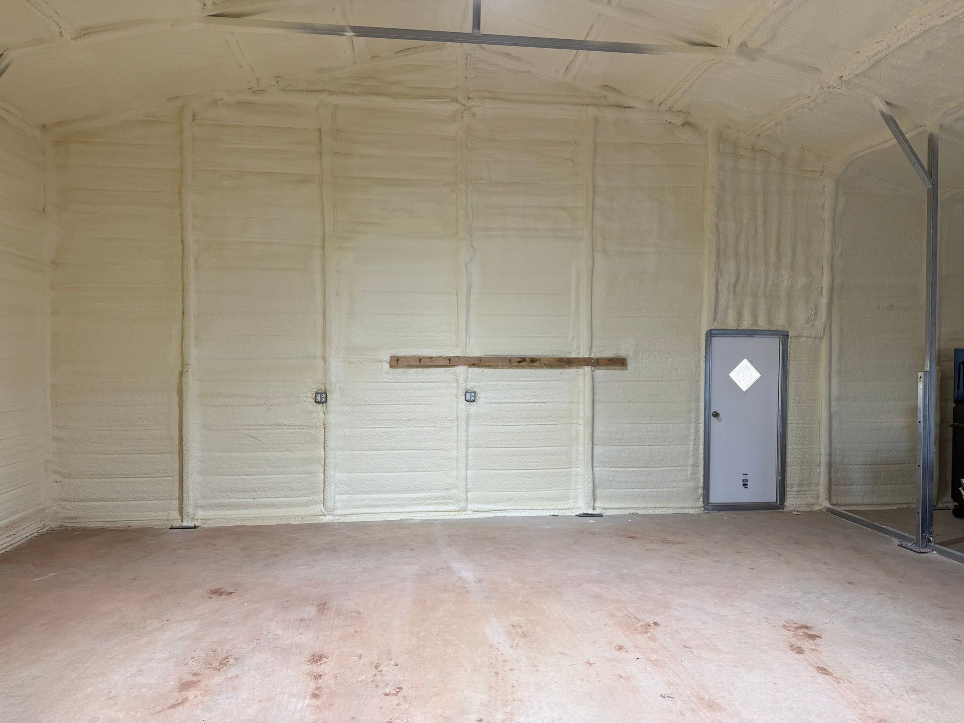 Interior view of a building with light brown spray foam insulation on walls and ceiling, including a door.
