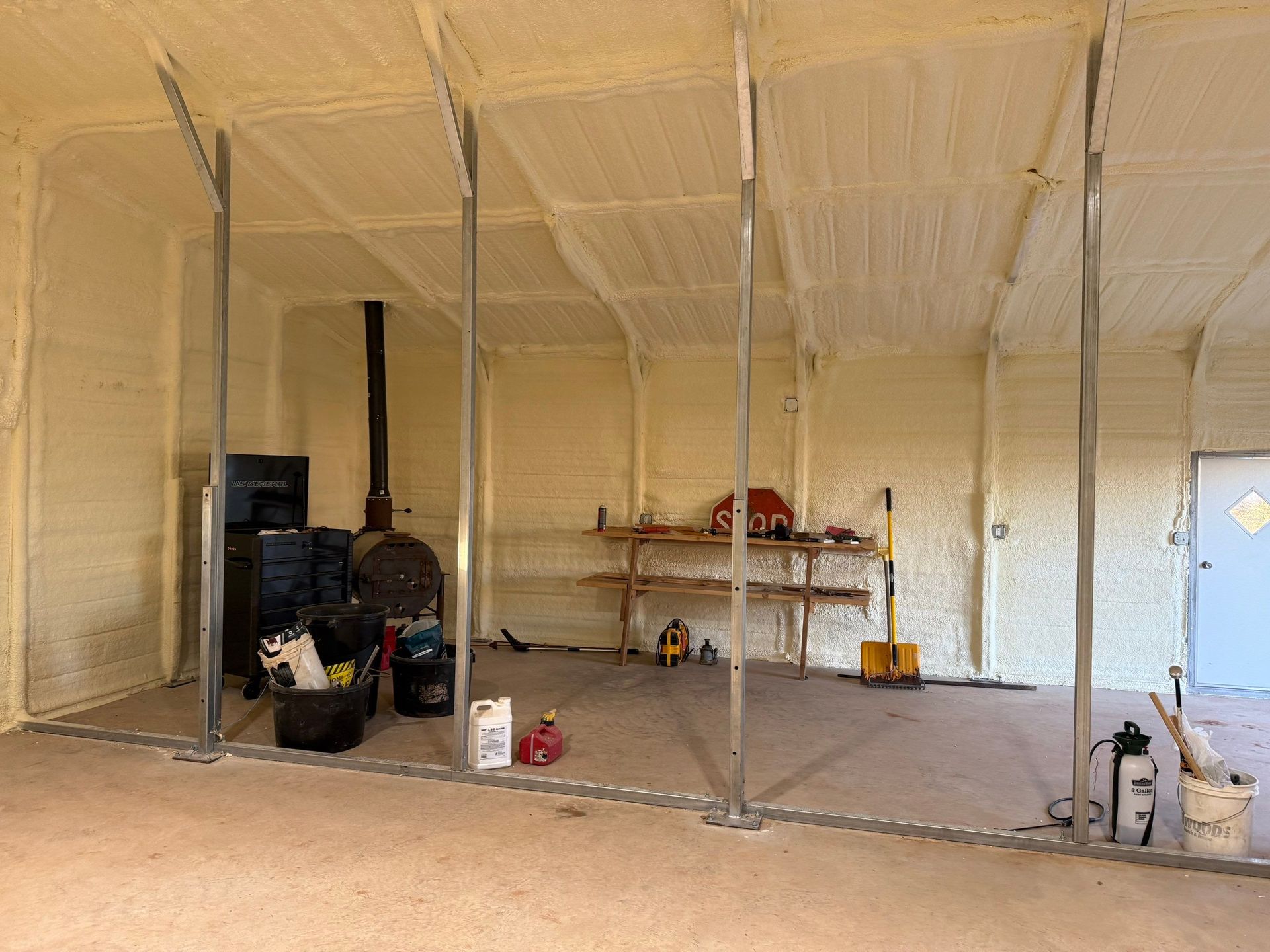 Interior of a building with spray foam insulation. Metal support beams and a concrete floor are visible.