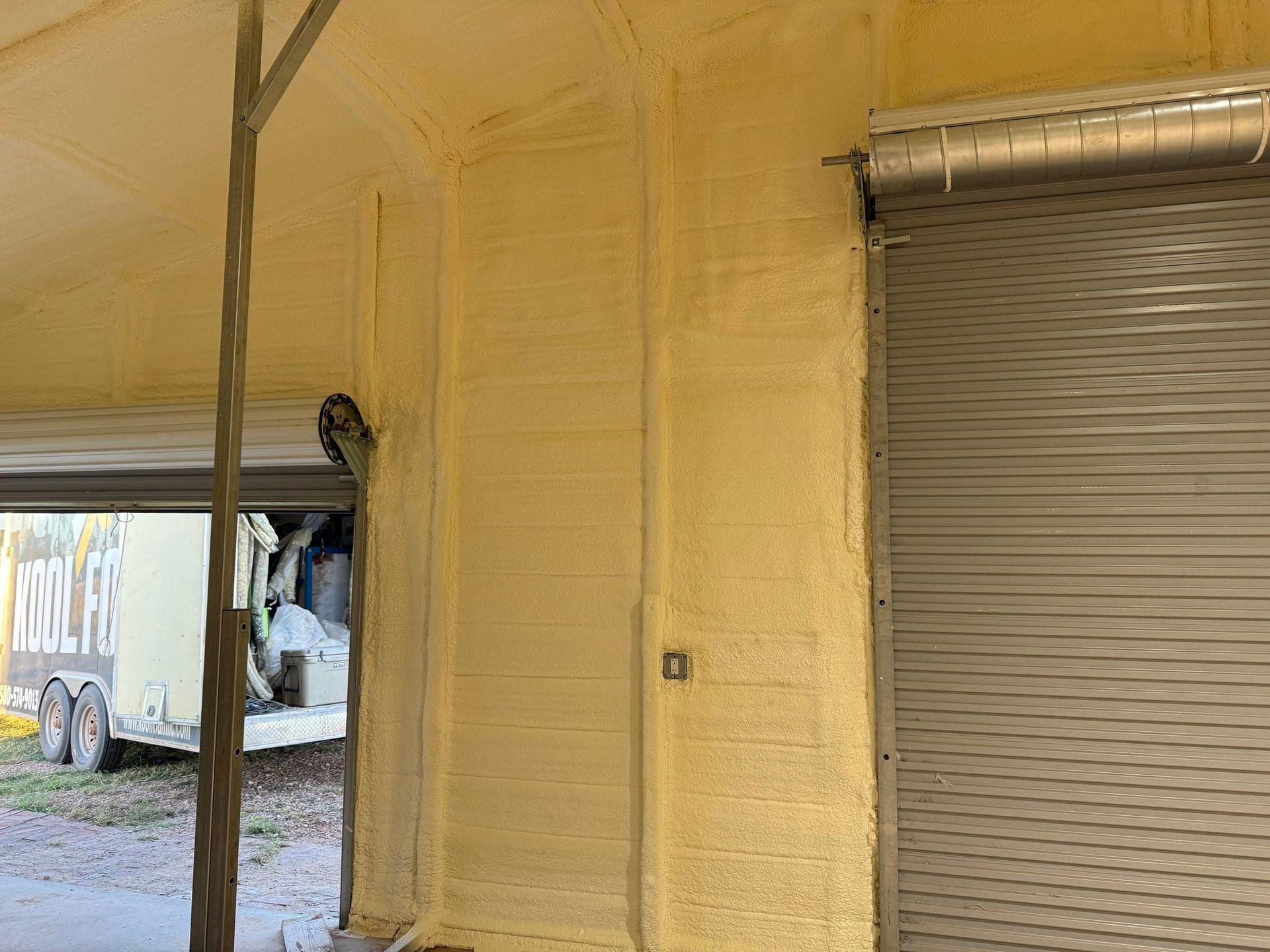 Yellow spray foam insulation on walls of a building with a rolling door and open bay.
