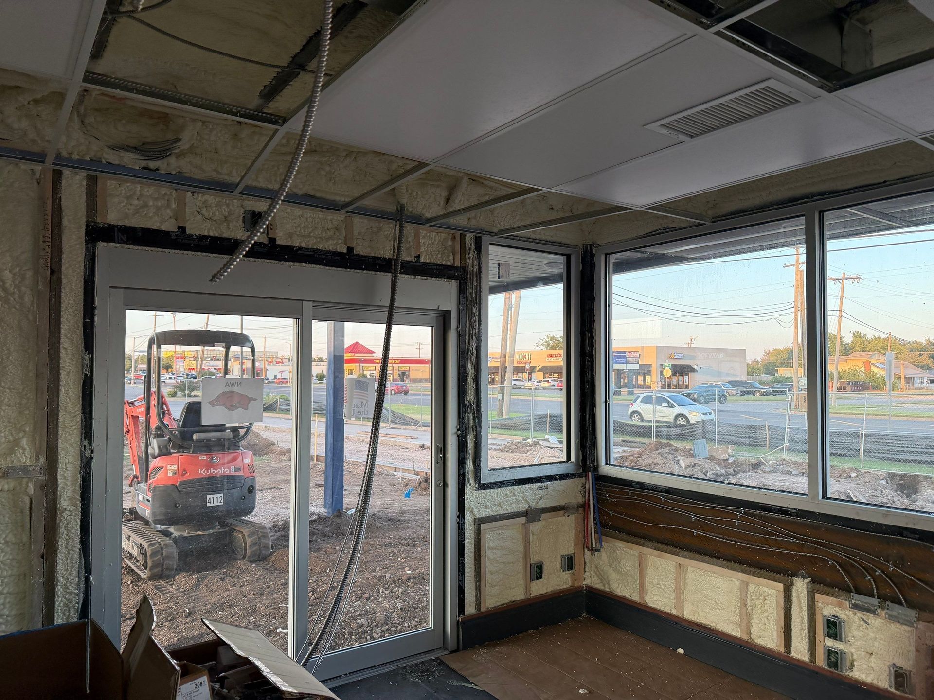 Interior construction site with door, windows, and small excavator outside.