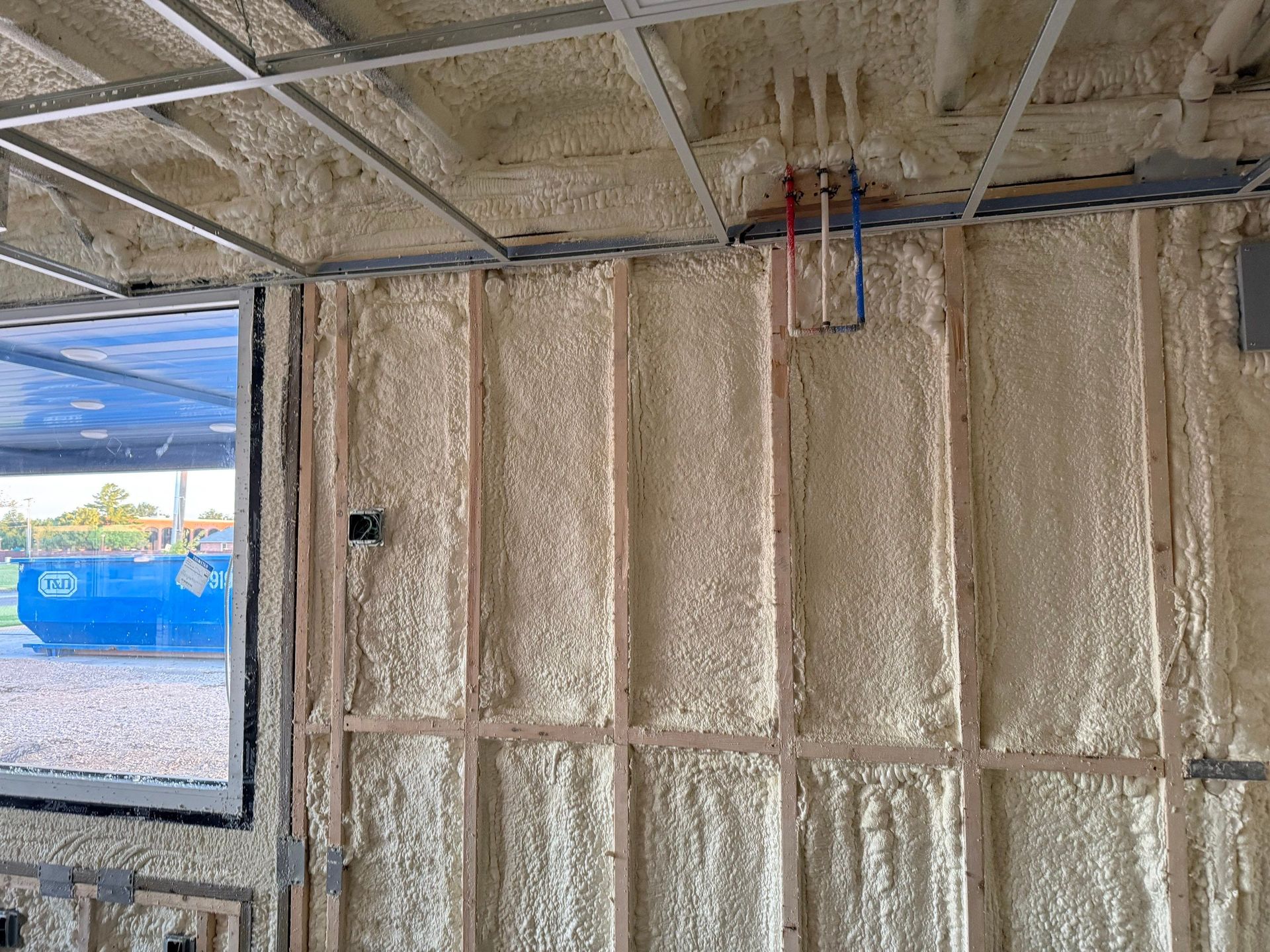 Interior view of a building's wooden frame walls and ceiling covered in spray foam insulation.