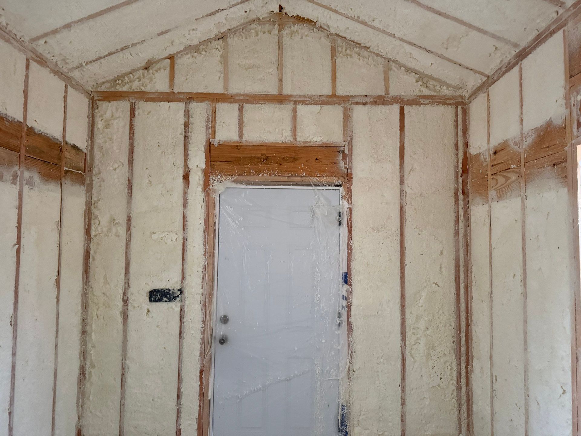 Interior of a wooden structure with walls insulated by spray foam. Door in the center.