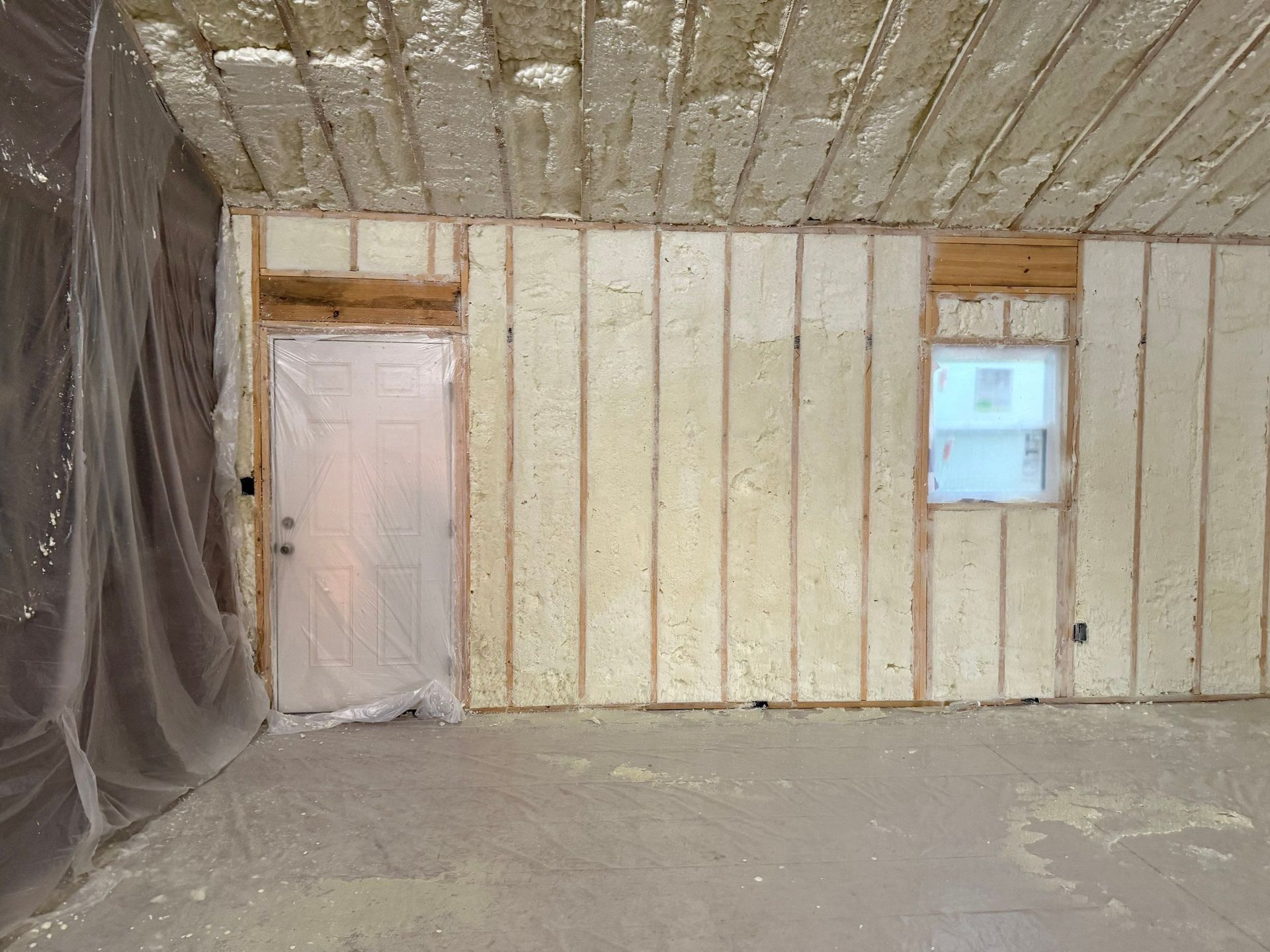 Interior room with insulation on walls and ceiling, including a door and window. The floor is covered.