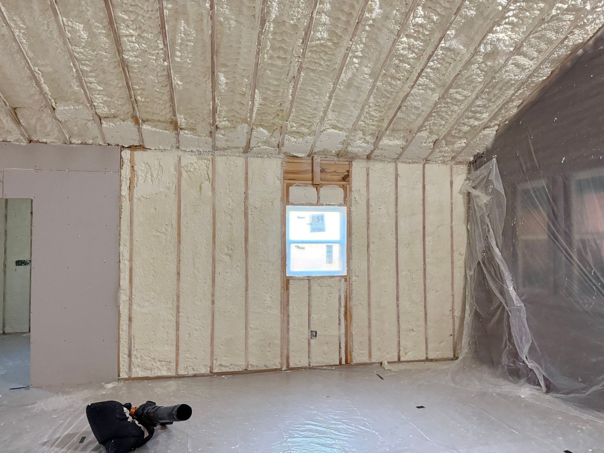 Interior room with spray foam insulation on walls and ceiling. Window in center. Person in foreground.