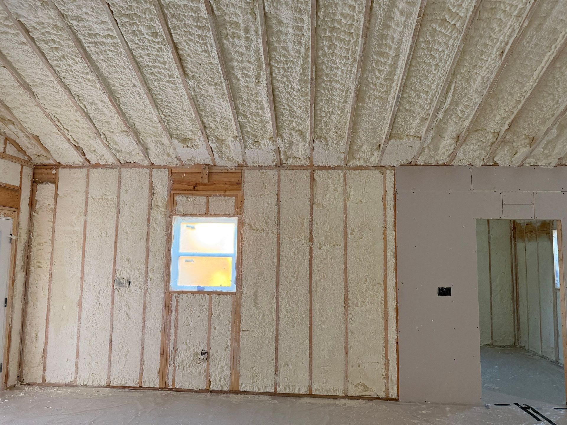 Interior of a building under construction, showing spray foam insulation on walls and ceiling.