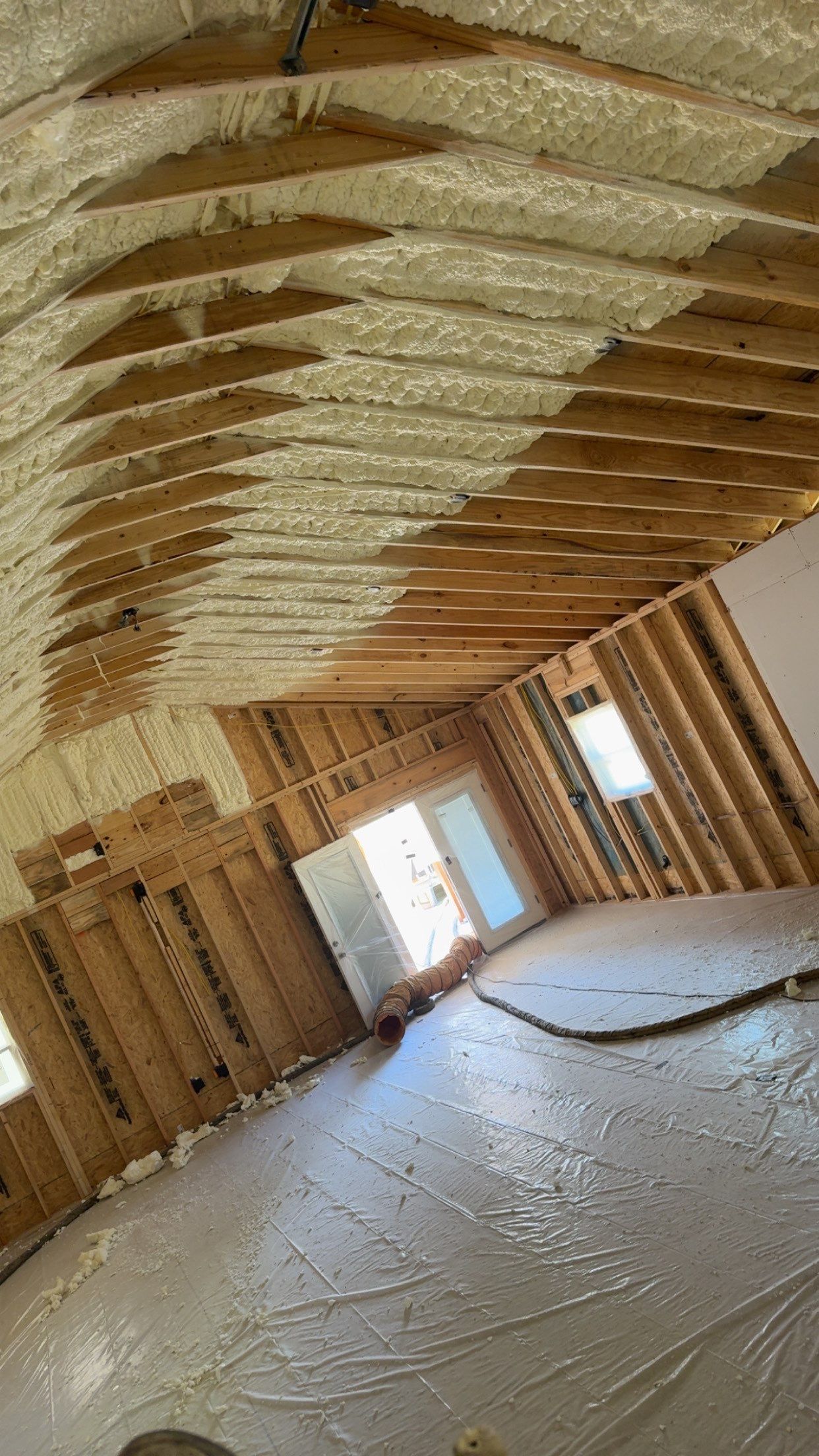 Interior view of a room under construction, with exposed wooden beams, insulation, and a door to the outside.