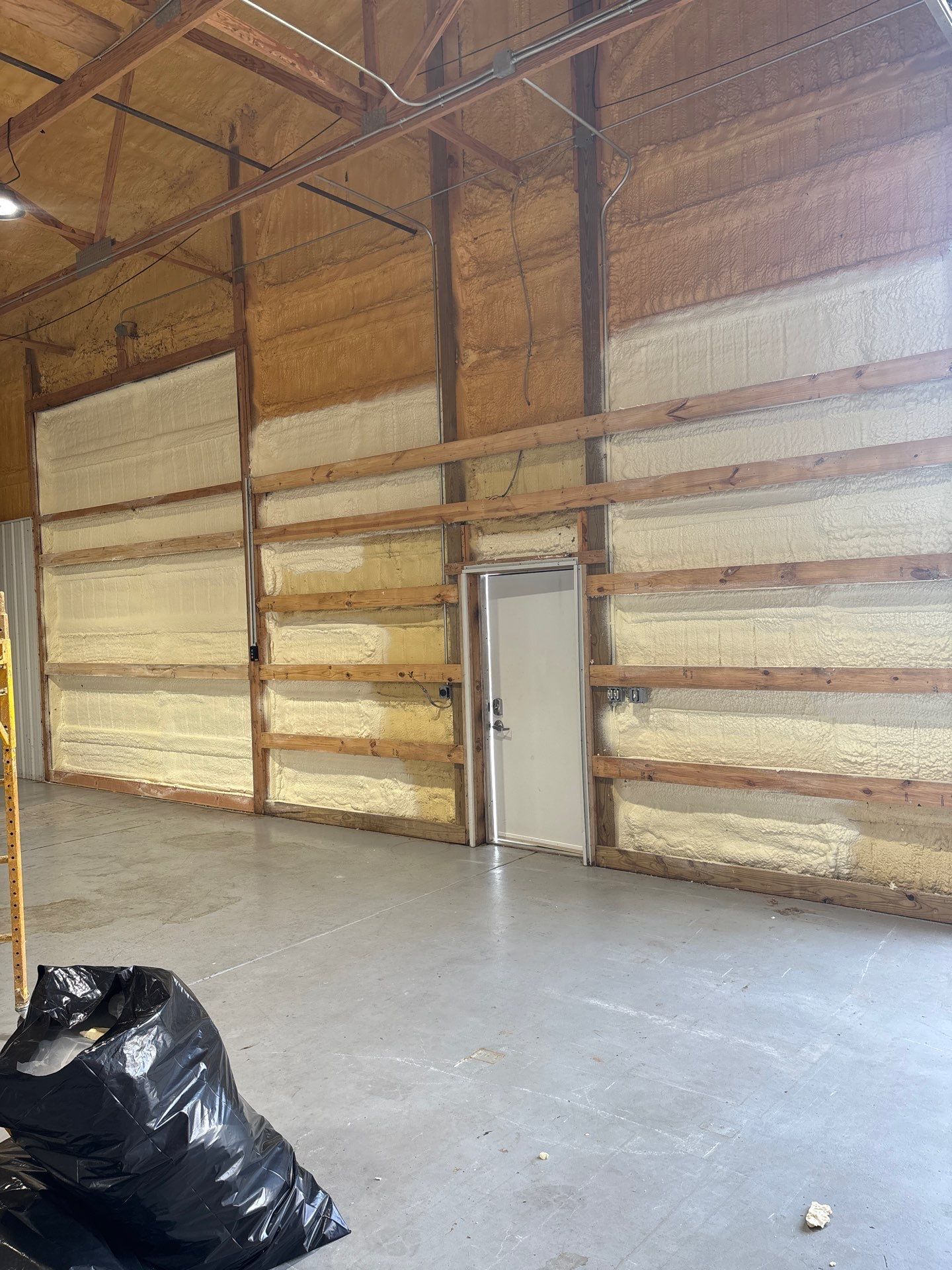 Interior of a building with spray foam insulation on walls and a concrete floor. A door is visible.