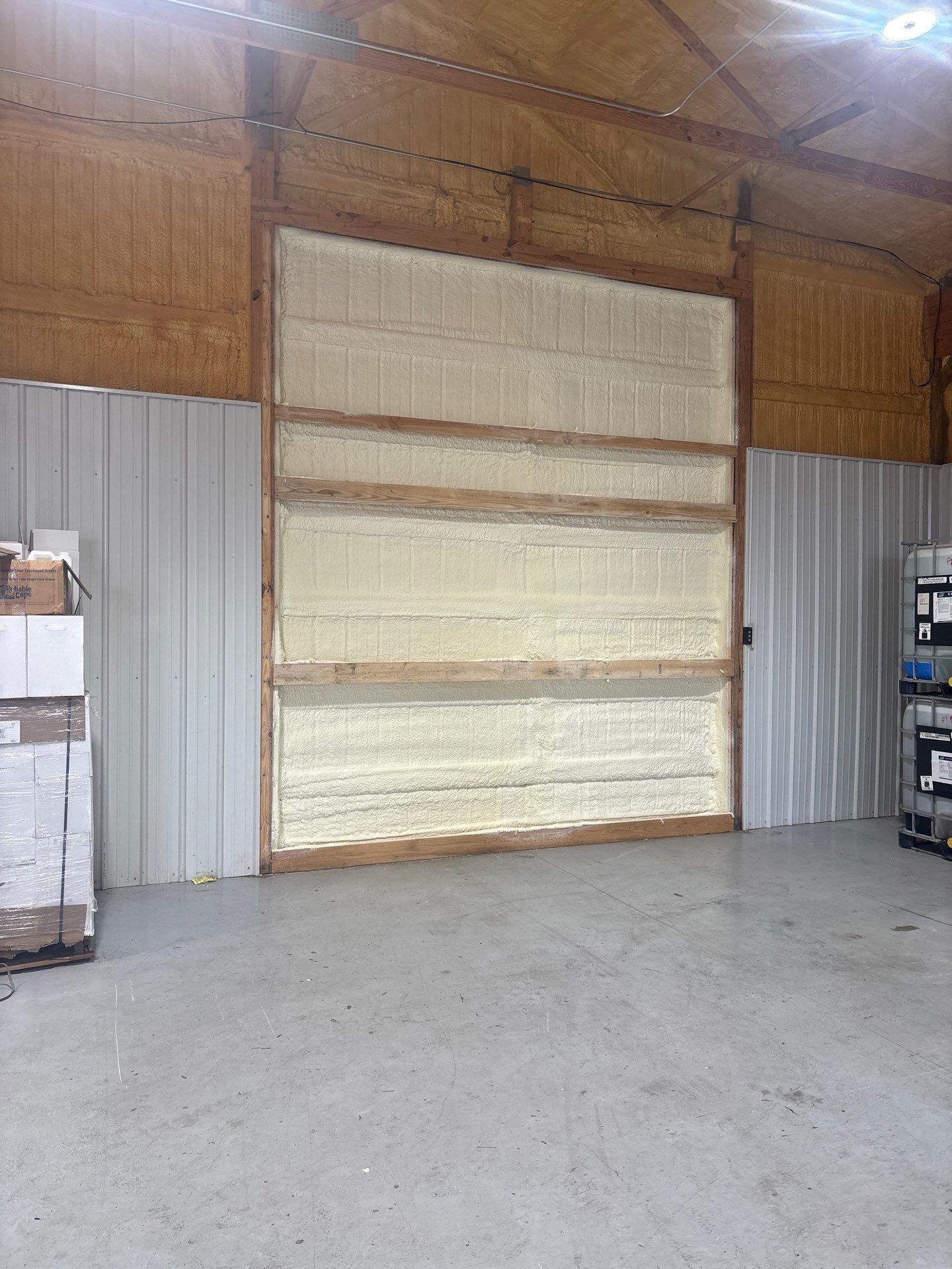 Interior of a building with a large opening filled with spray foam insulation. Metal siding and wooden beams are visible.