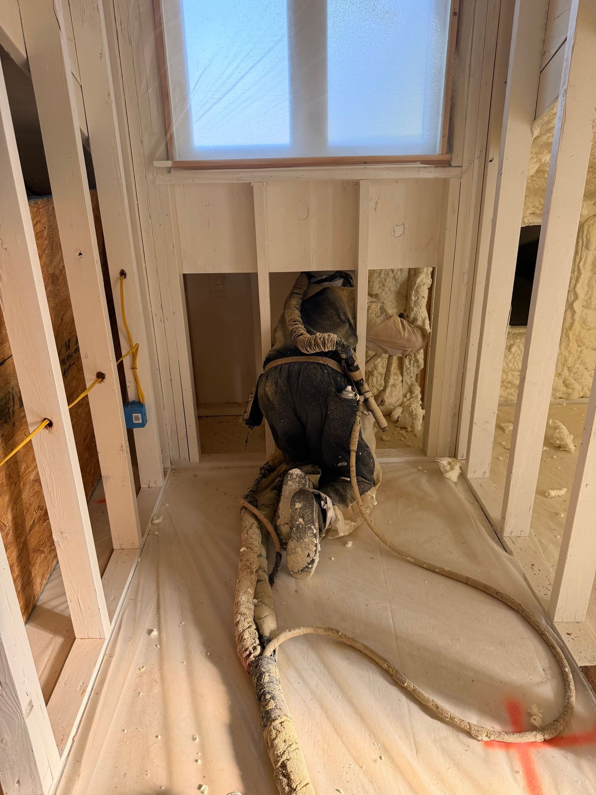 Interior framing with spray foam insulation, window, and electrical wiring.