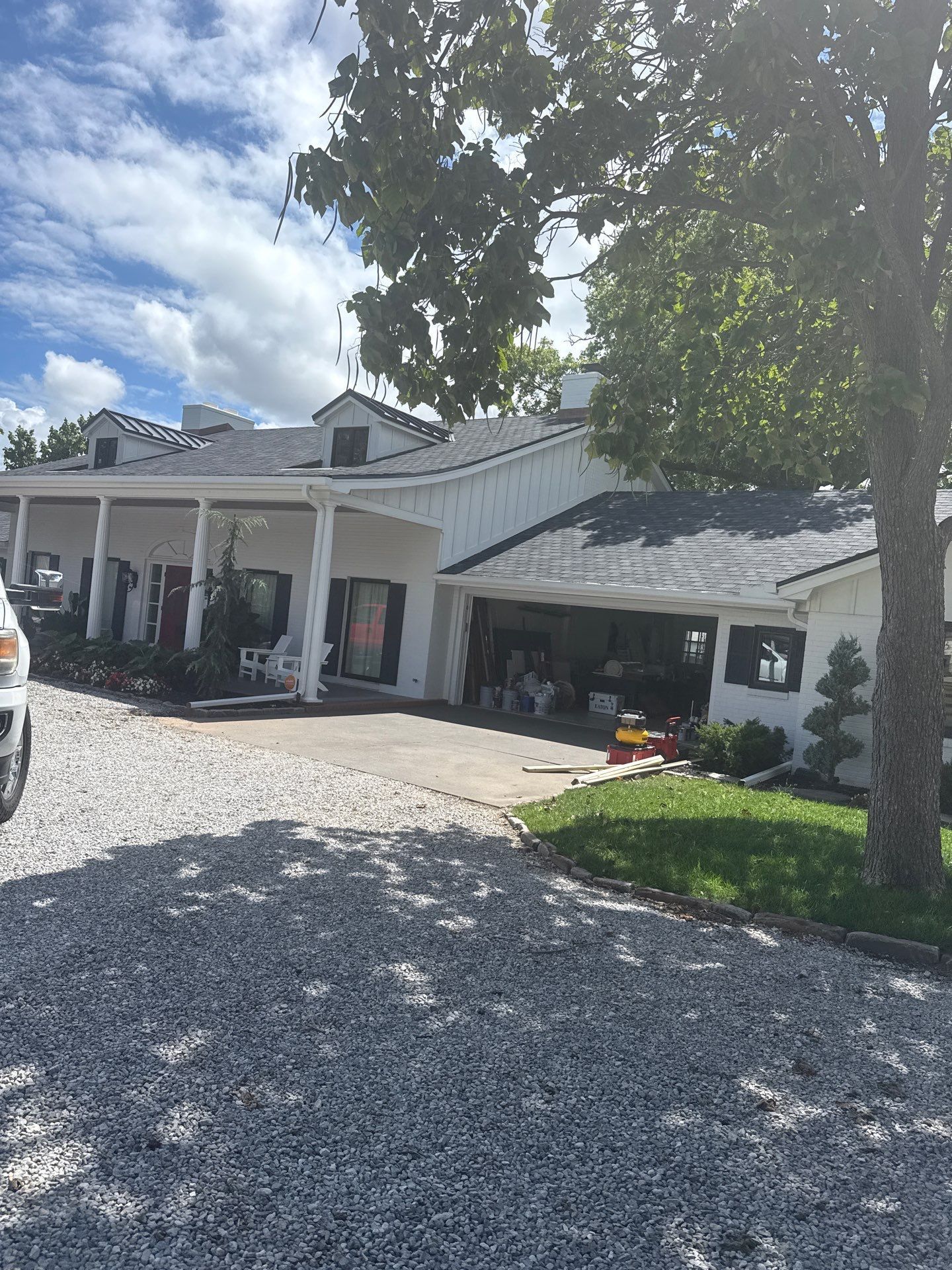 White building with dark roof under a partly cloudy sky, gravel driveway, and a tree on the right side.