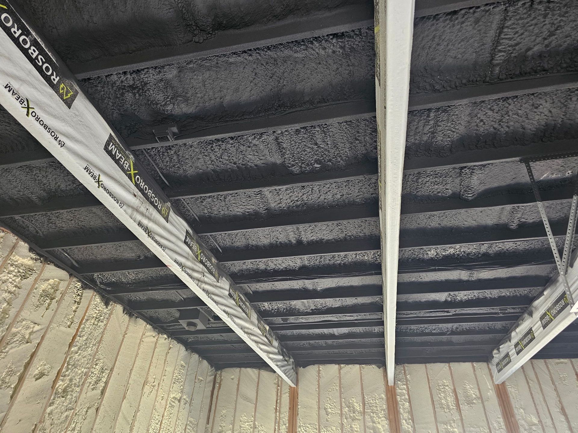 Black spray foam insulation on ceiling with exposed wooden beams.