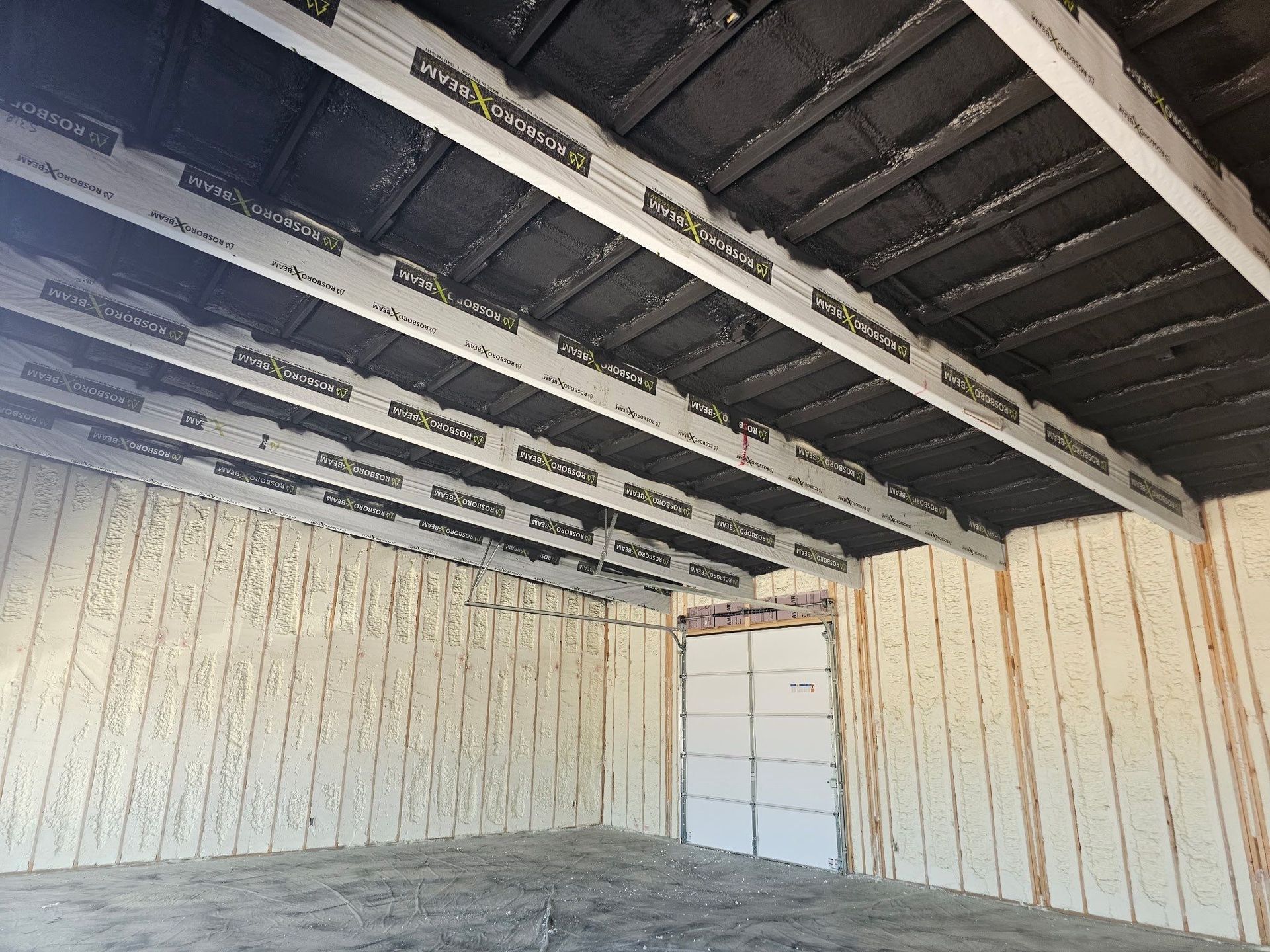 Interior view of a room with spray foam insulation on ceiling and walls, and white beams.