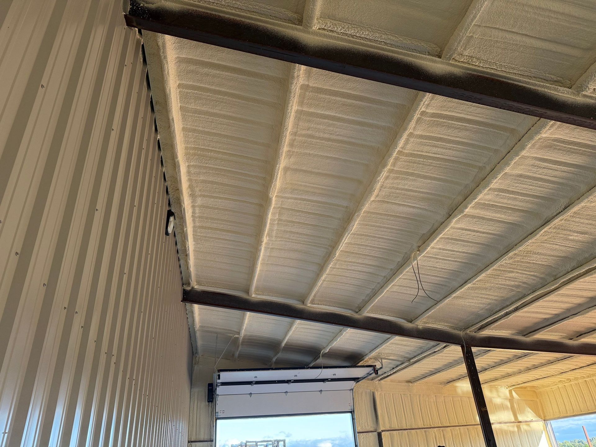 Spray foam insulation on a corrugated metal ceiling and wall, beige and brown tones.