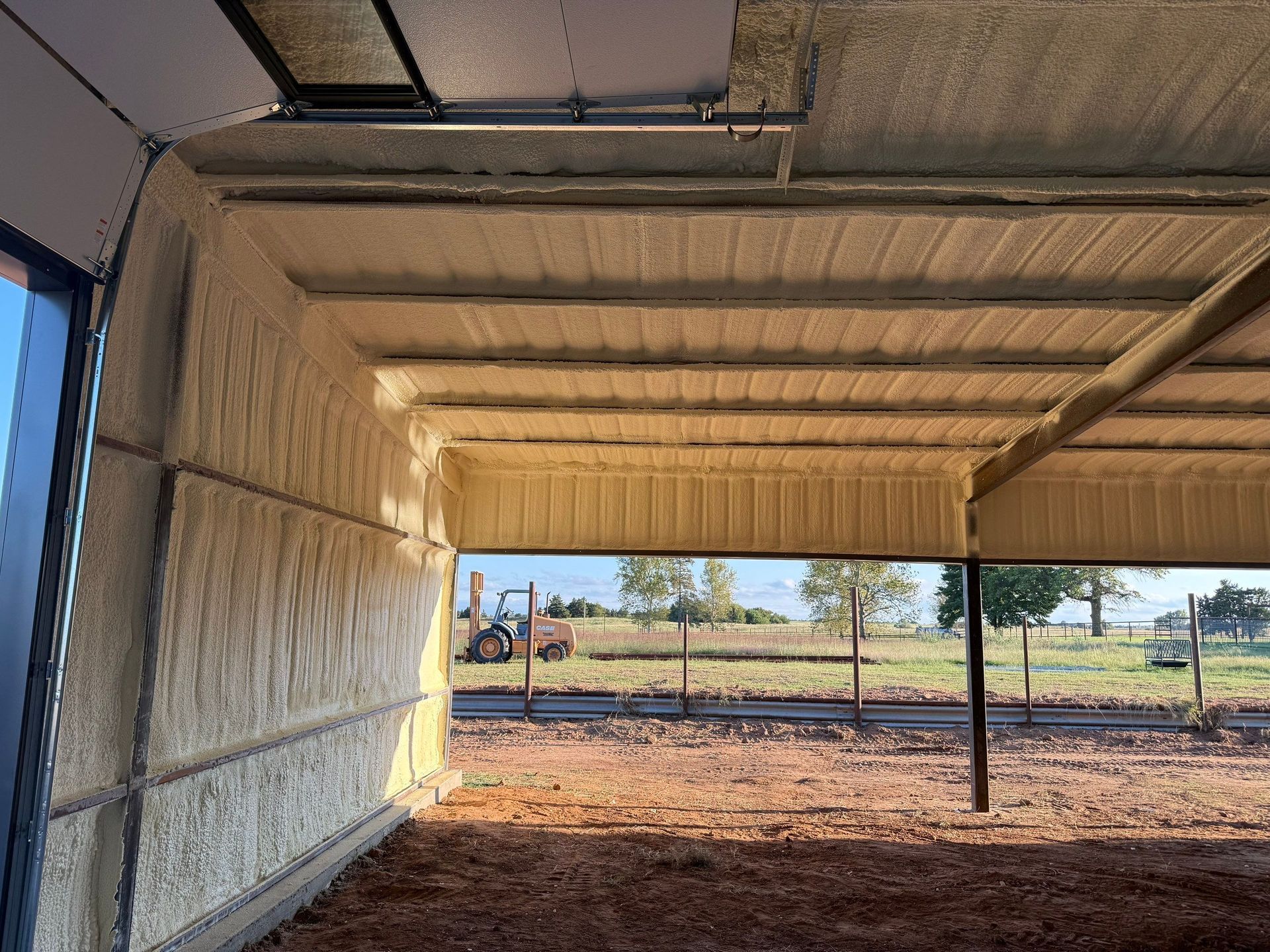 Interior of a building with spray foam insulation; exterior view through an opening of a field and a tractor.