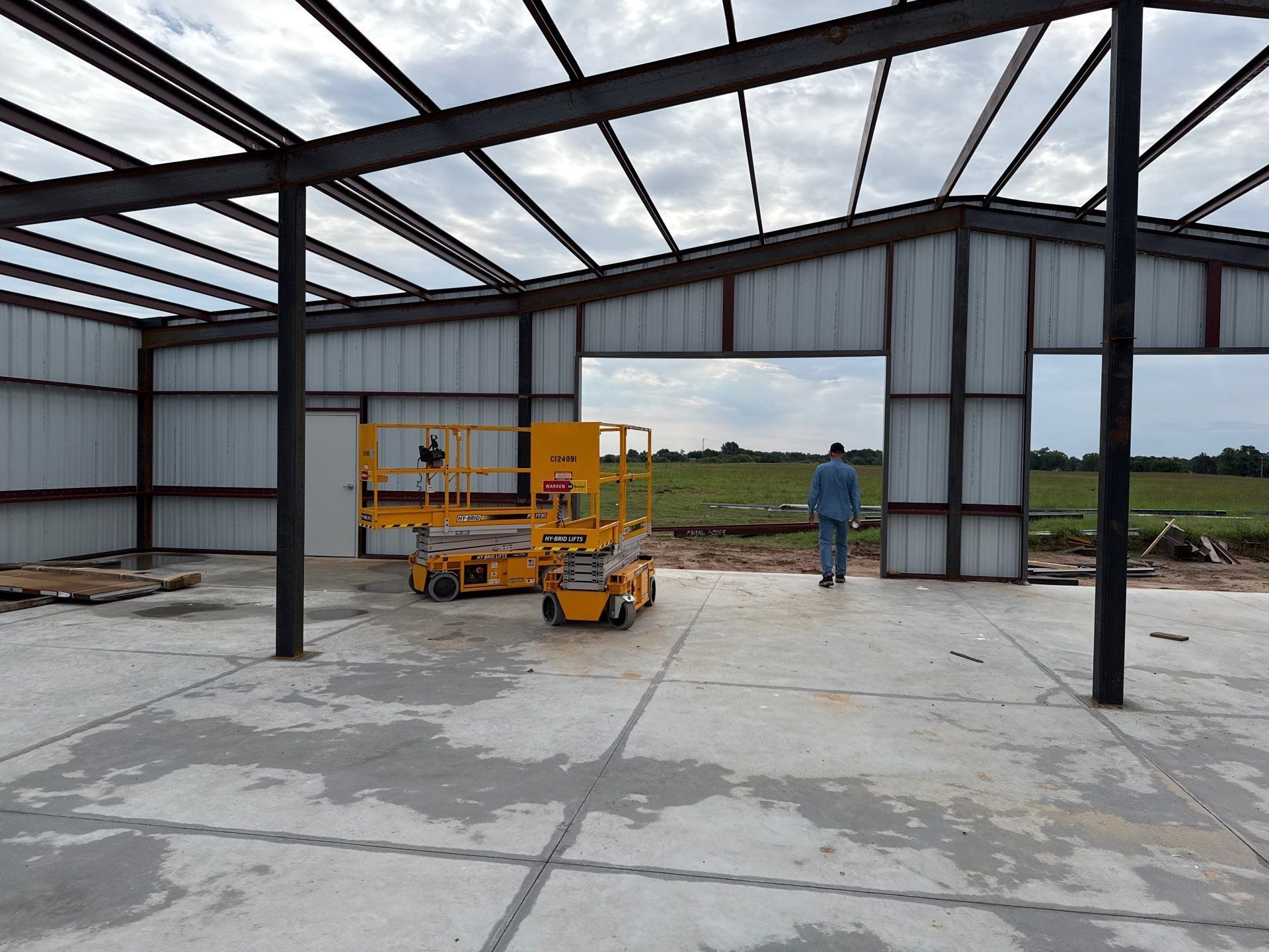Metal frame building under construction, yellow lift, person walks outside.