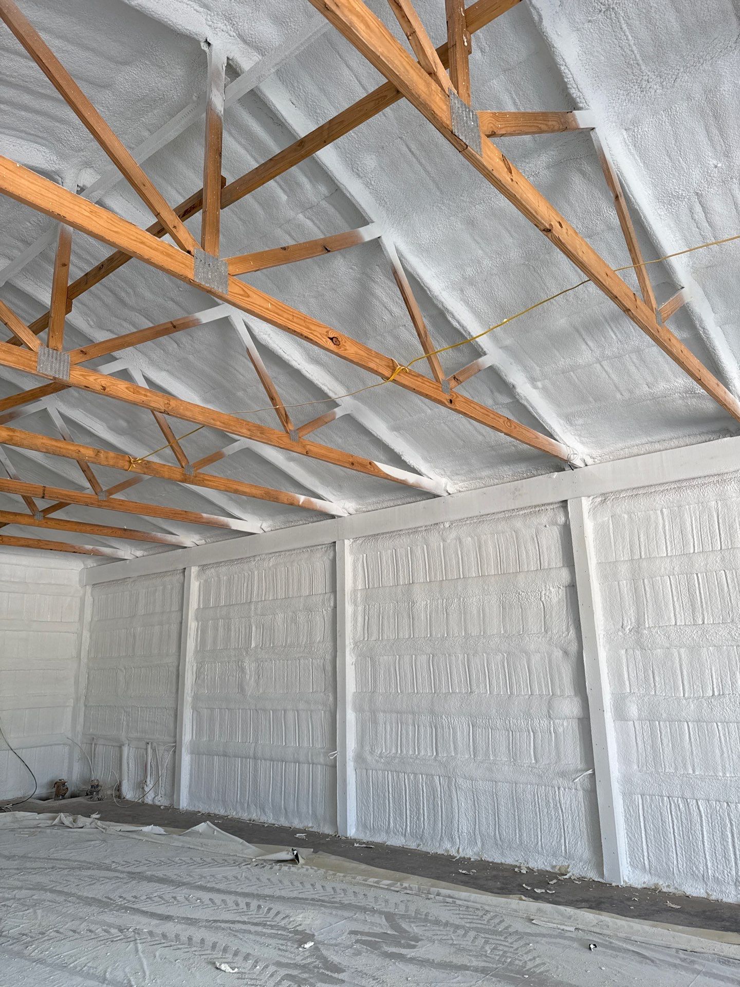 Interior view of a building with spray foam insulation on the walls and ceiling. Wooden beams support the roof.