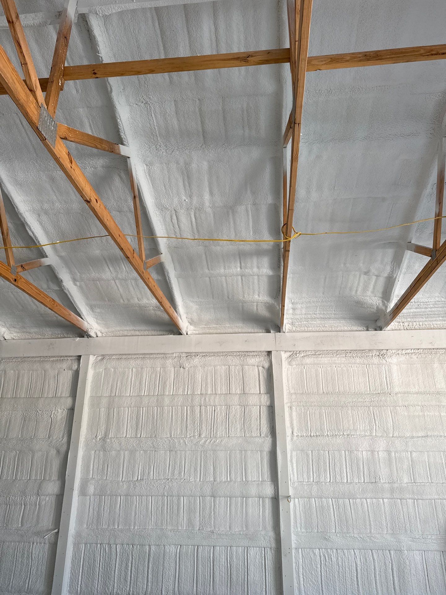 White spray foam insulation on ceiling and walls of a building with wooden beams.