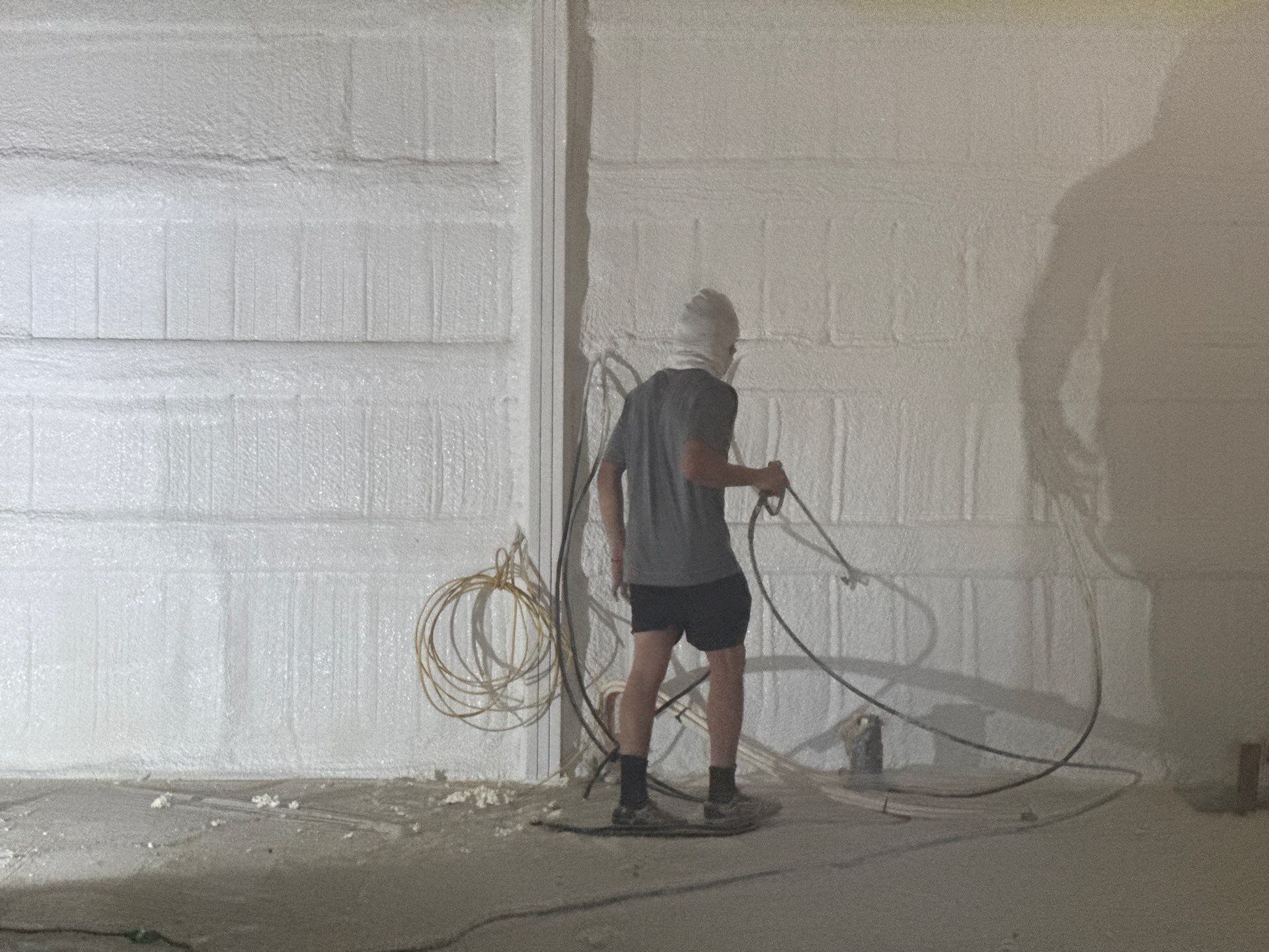 A person spraying insulation foam on a wall, in a building with concrete floors.