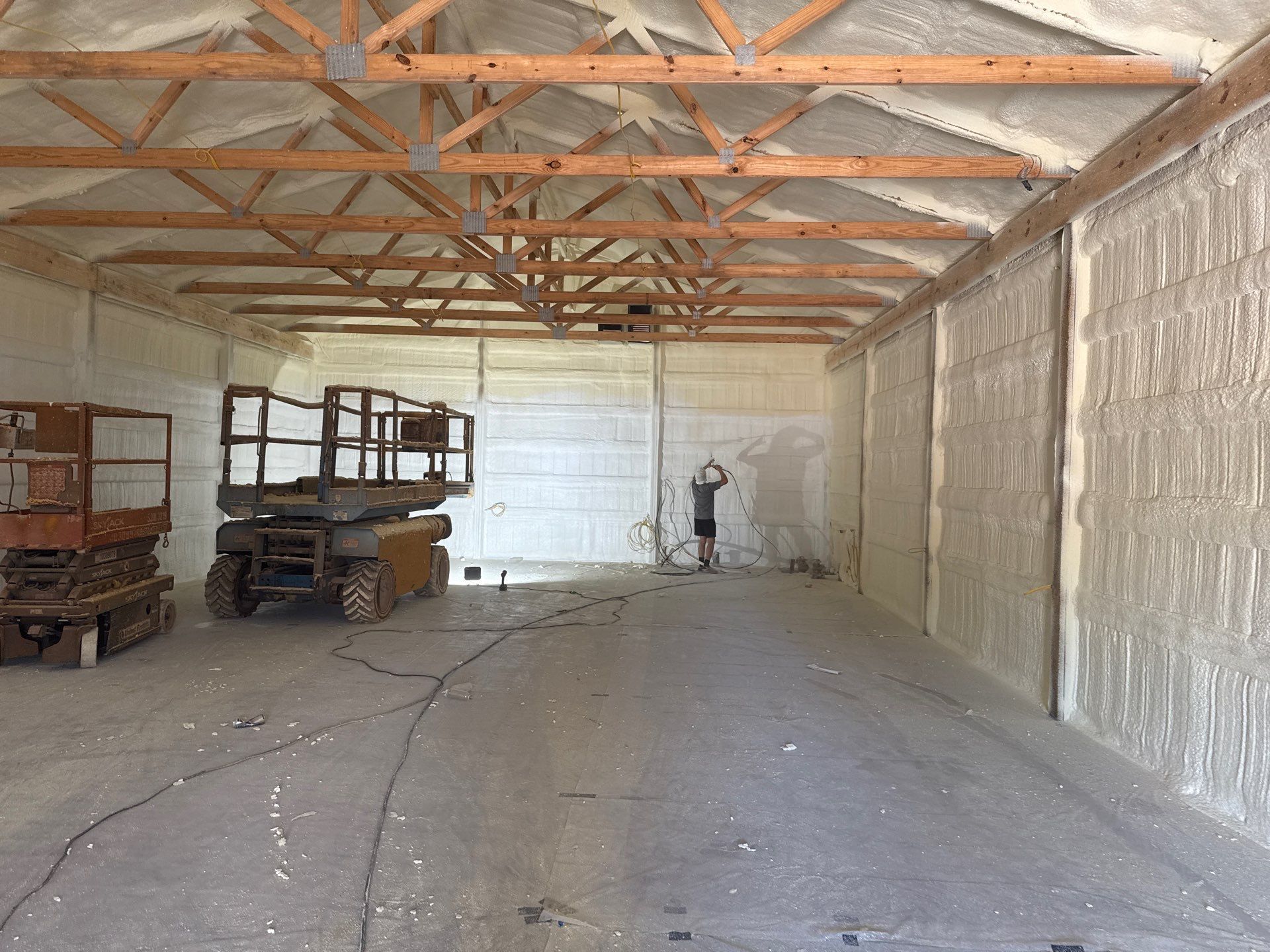 Interior of a building with spray foam insulation on walls and ceiling. Person standing in center. Two lifts on left.