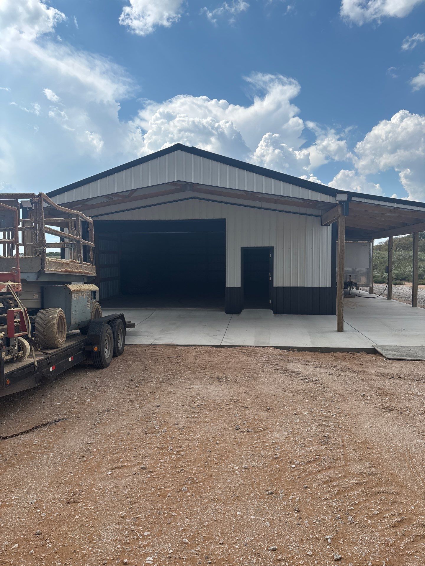Metal building with open bay doors under a blue sky, gravel lot in front.