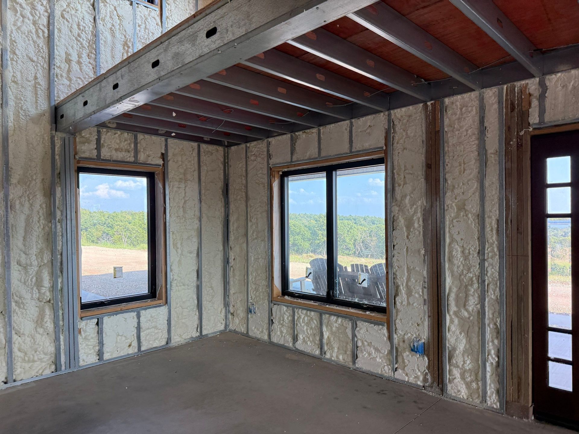 Interior of a building with spray foam insulation visible on walls and ceiling, windows and door are in place.