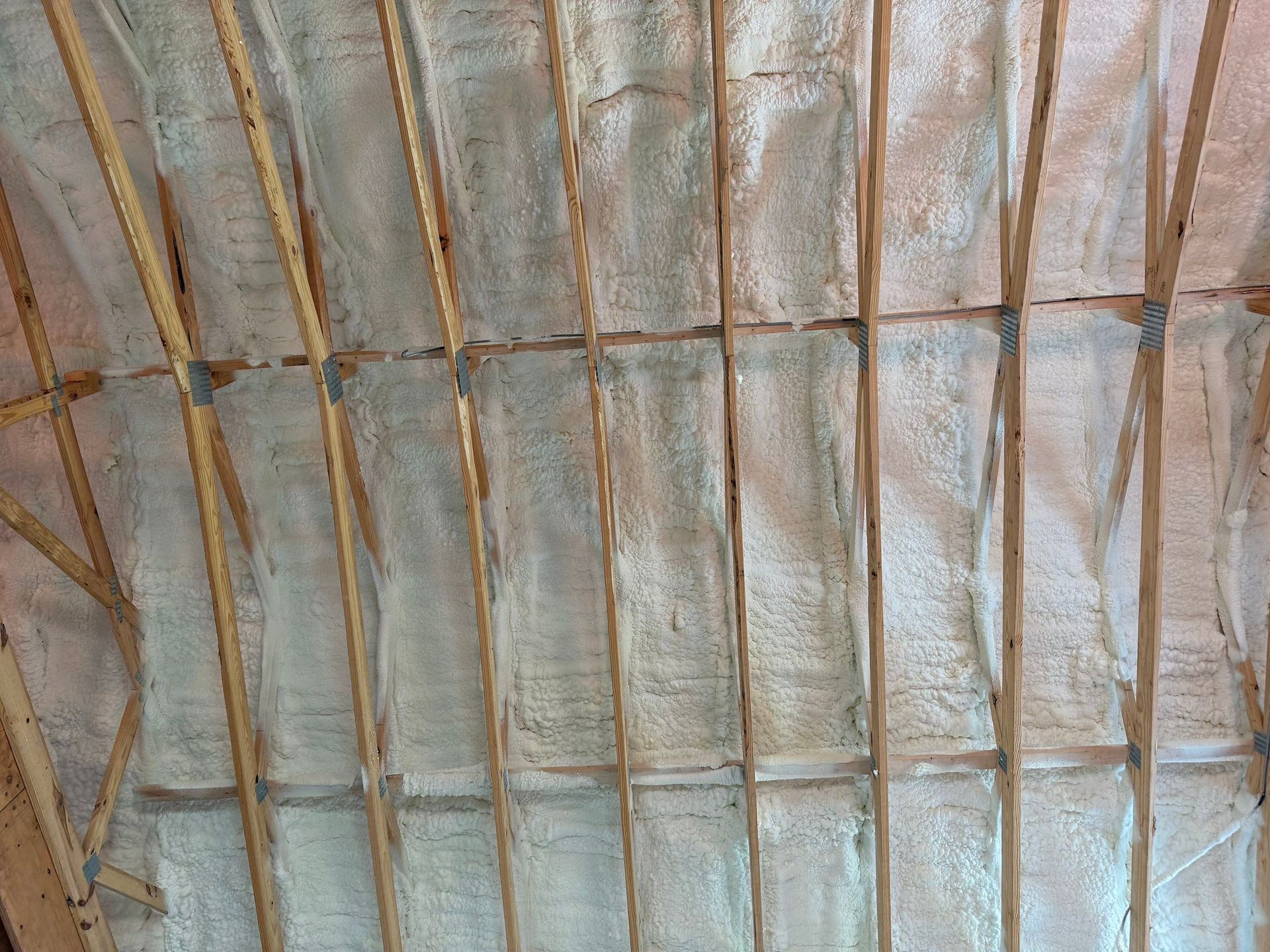 Wooden roof trusses with white spray foam insulation.
