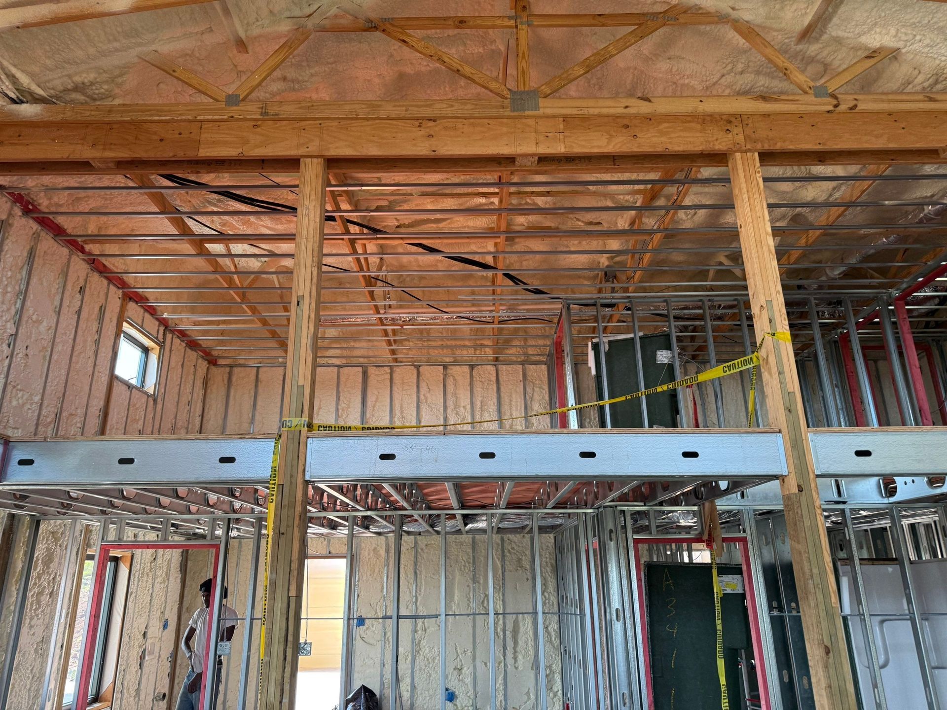 Interior of a building under construction, showing framing, insulation, and exposed wiring.