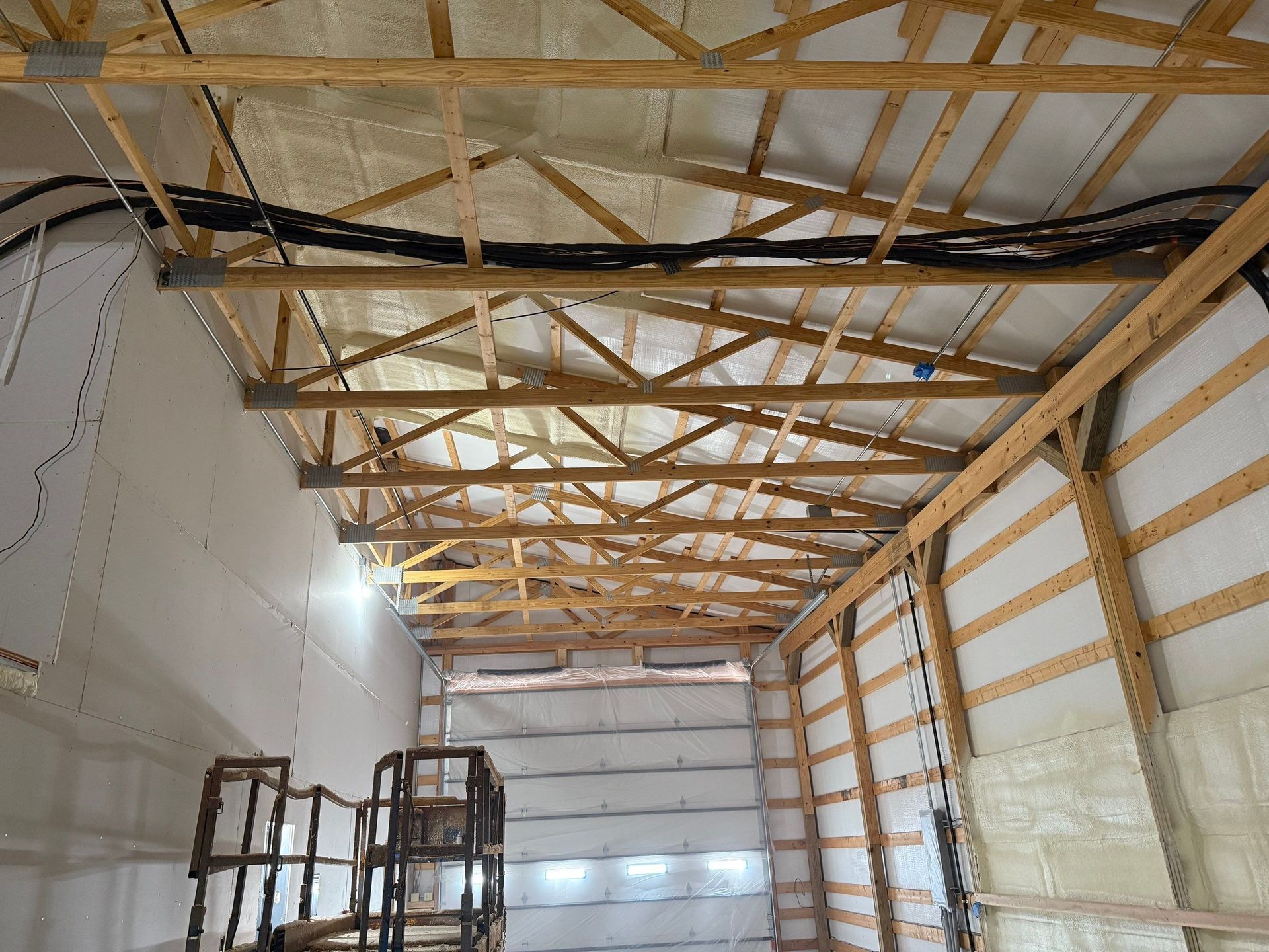 Interior view of a building under construction, showing wooden rafters, insulation, and electrical wiring.