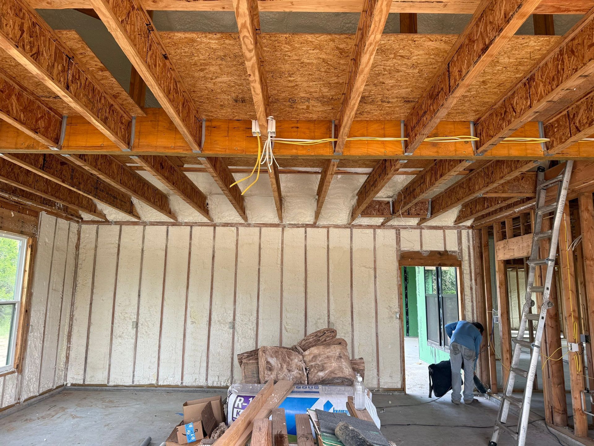 Interior of a building under construction, walls and ceiling insulated with foam, a person in the doorway.