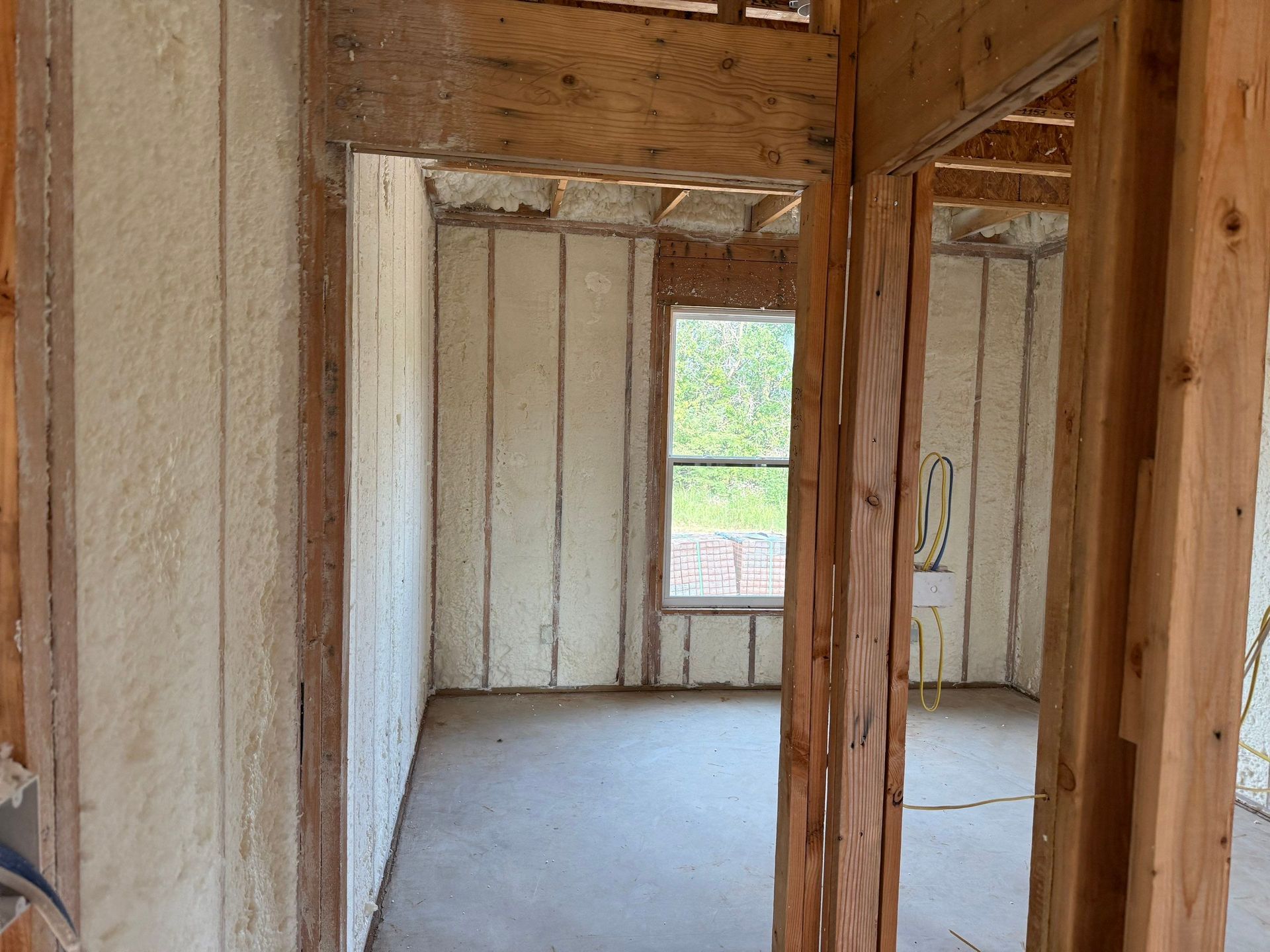 Interior of a room under construction, walls sprayed with insulation; window in far wall.