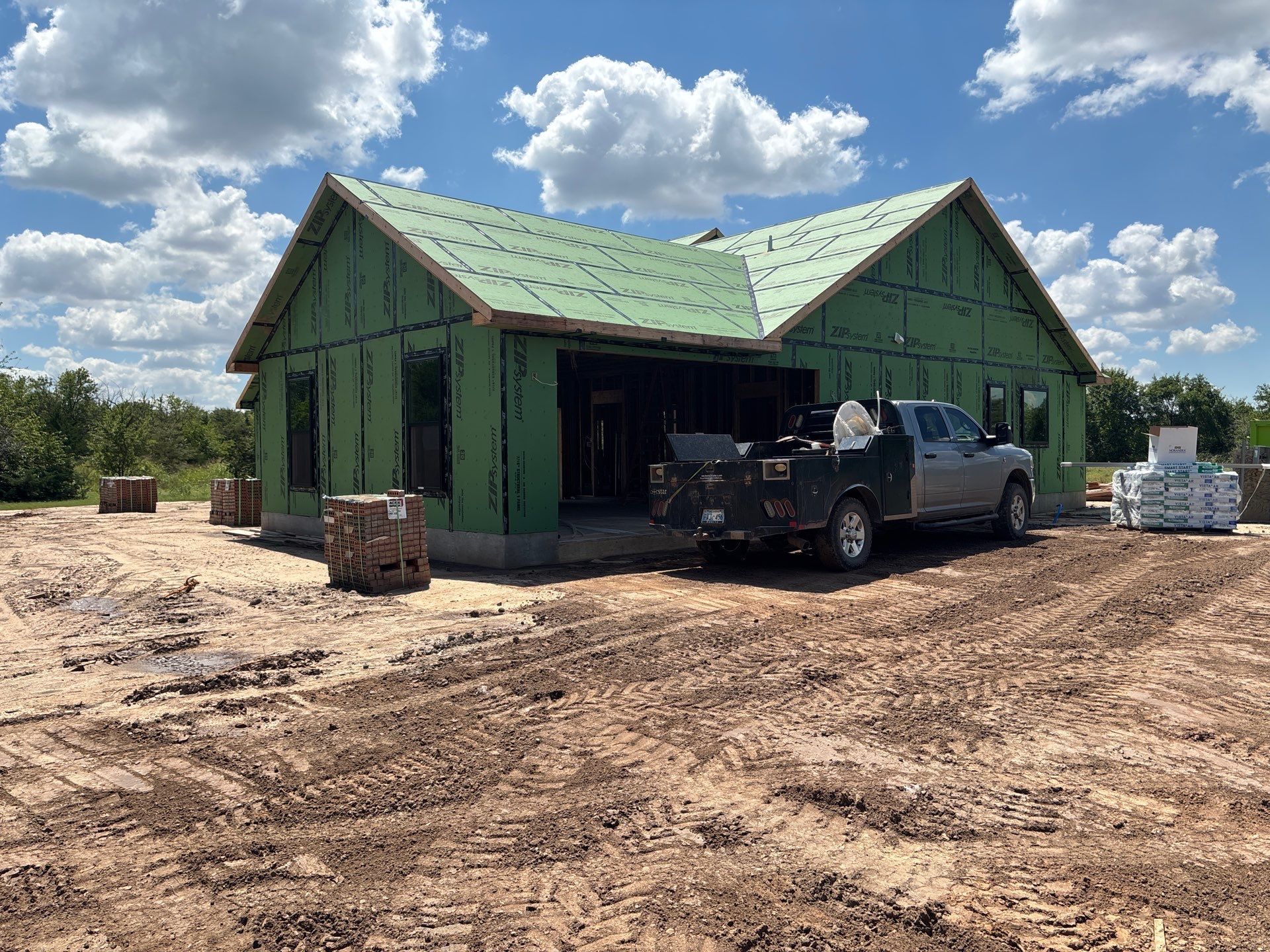 House under construction with green exterior, truck parked in front on dirt.