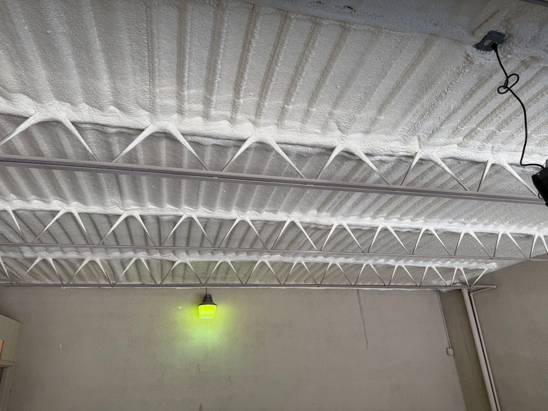 Ice formations hang from a ribbed metal ceiling, with a green light illuminating a wall below.