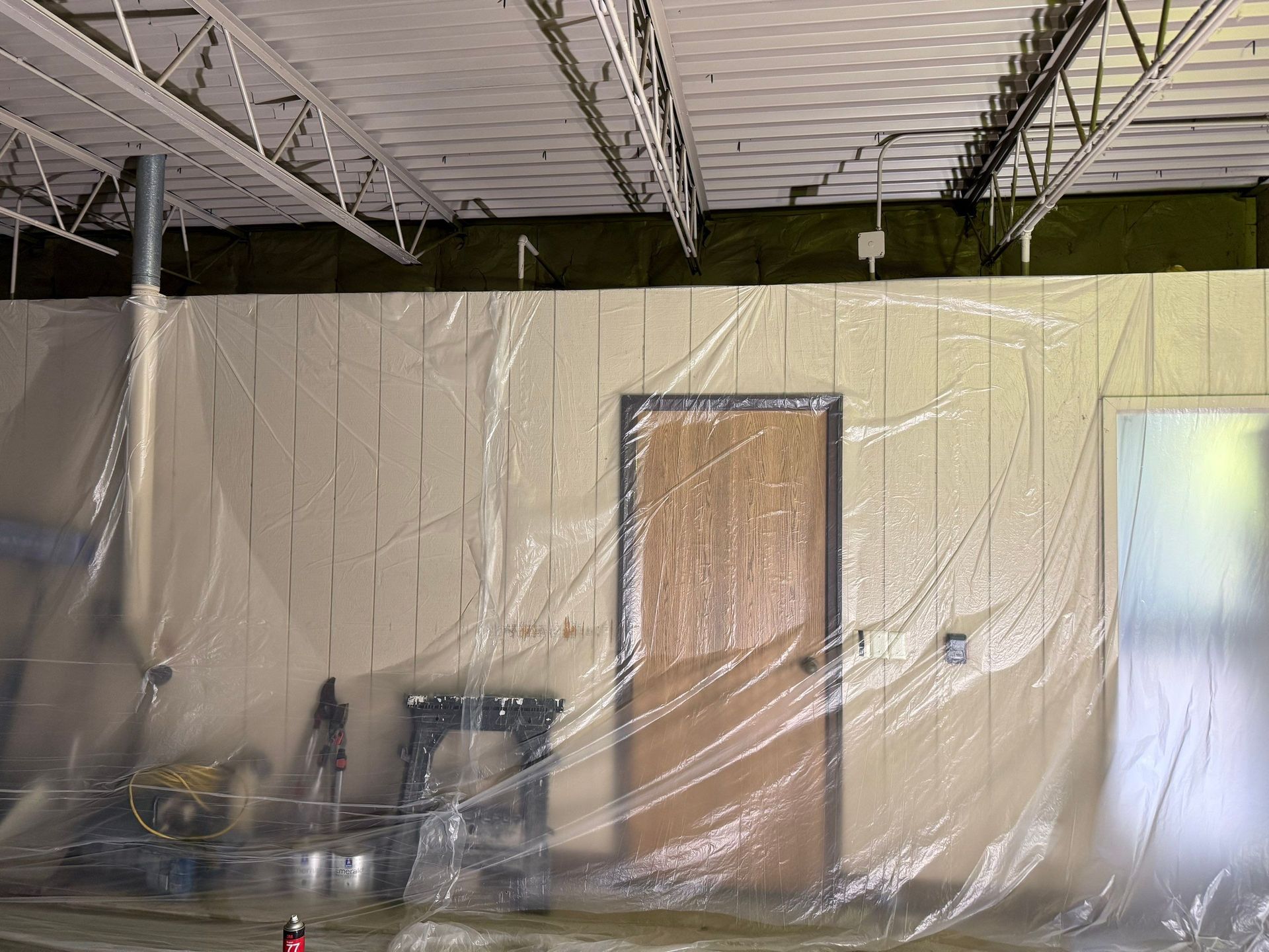 Interior space with plastic sheeting covering walls and a door, likely for protection during work.
