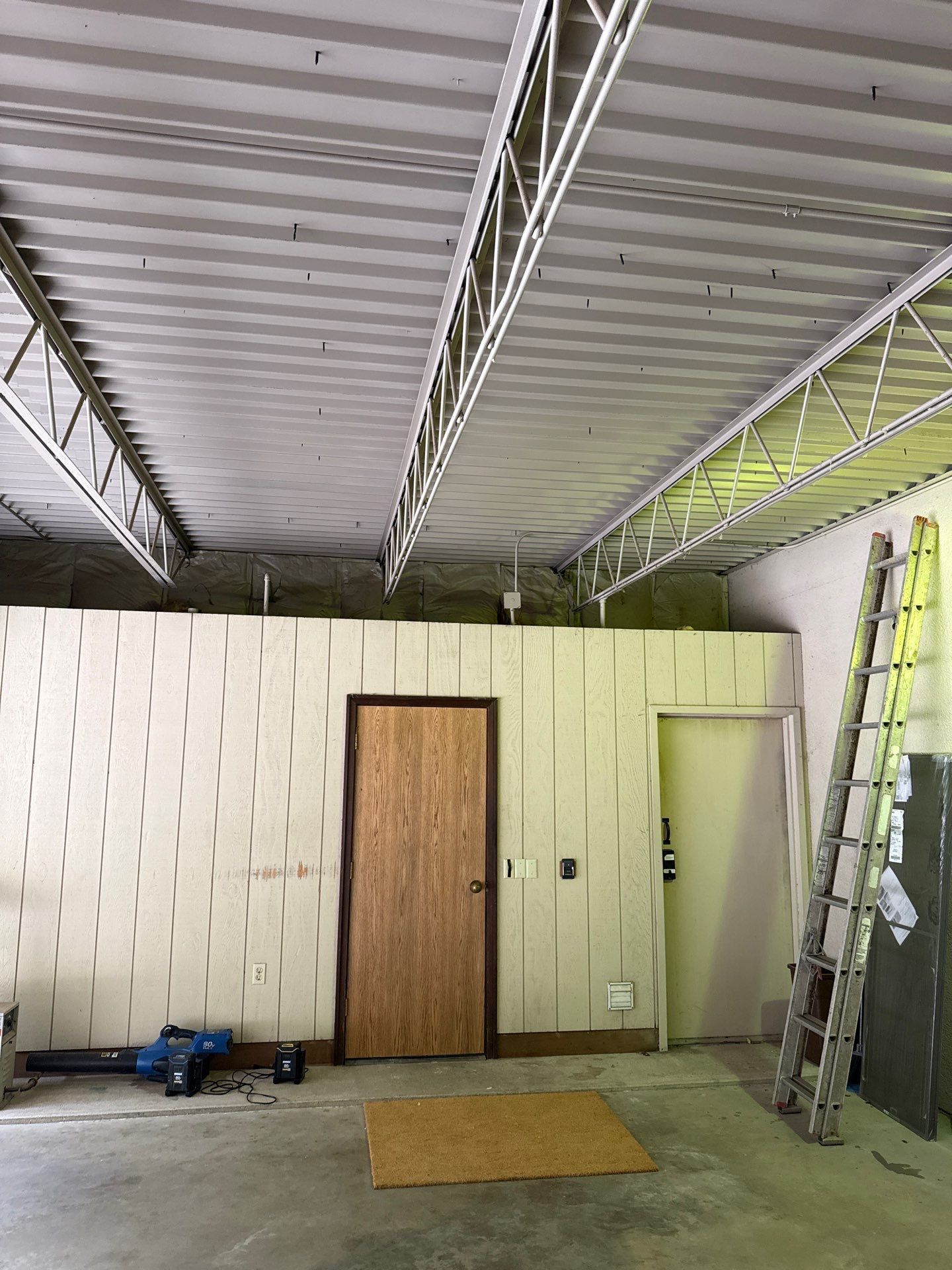 Interior view of a construction site with exposed ceiling, walls, doors, and a ladder.