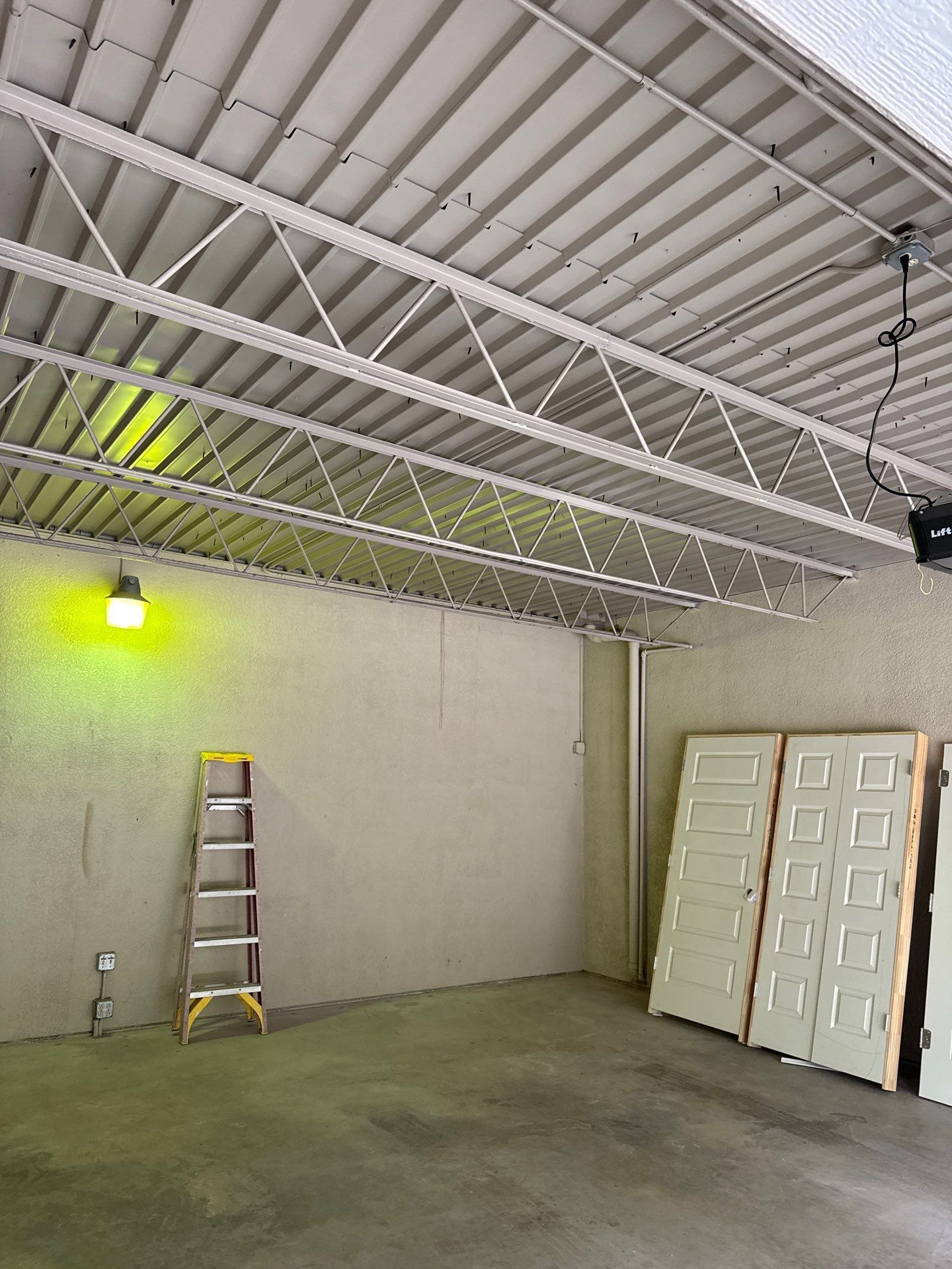 Interior of a garage with a metal roof. A ladder stands against the wall, with doors leaning against the right wall.