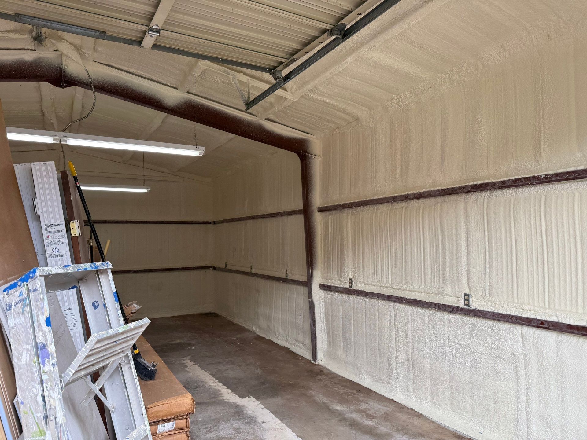 Interior of a metal building with spray foam insulation on walls and ceiling. Brown beams and a concrete floor.