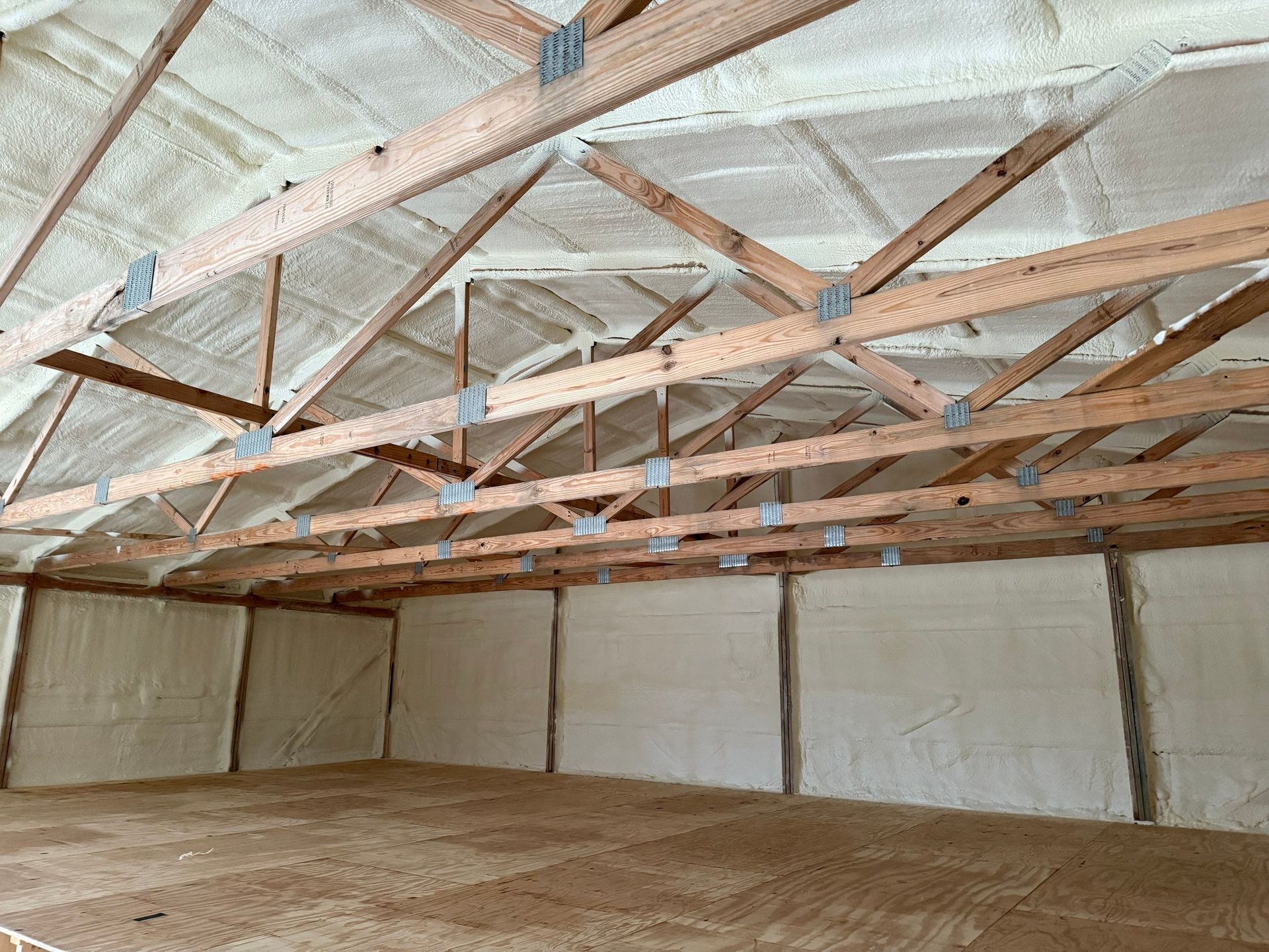Interior of a building with exposed wooden trusses and walls and ceiling covered in white spray foam insulation.