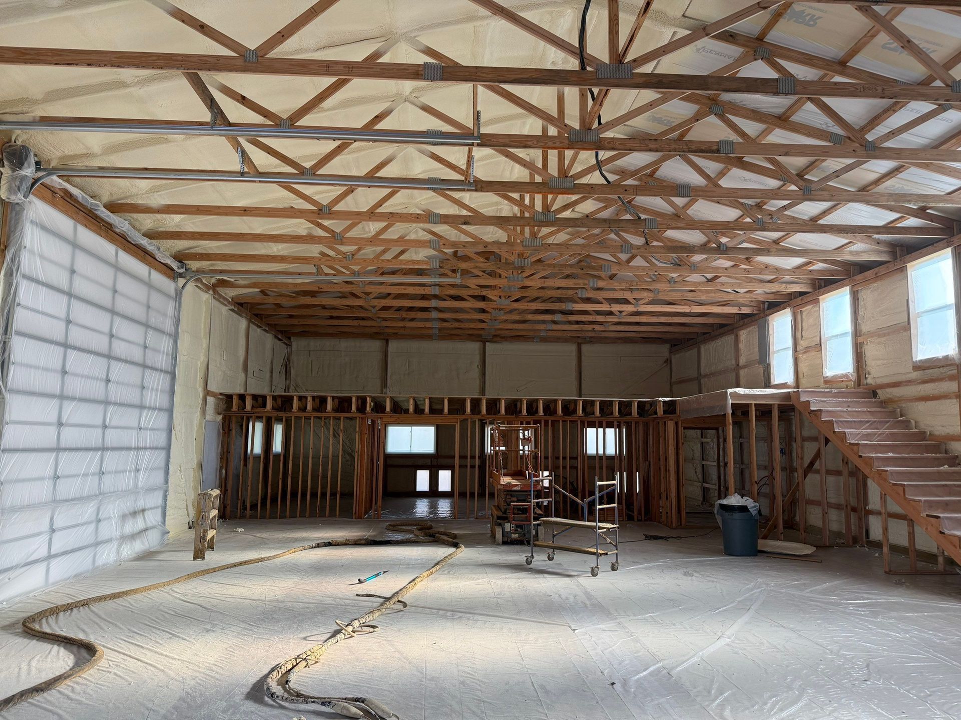 Interior view of a building under construction, featuring wooden framework, spray foam insulation, and a partial staircase.