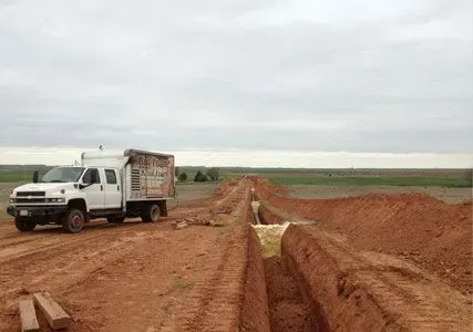 White truck next to a trench, construction in a field, under a cloudy sky.