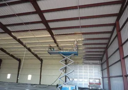 Interior of a building with spray foam insulation being applied to the ceiling by a worker on a lift.