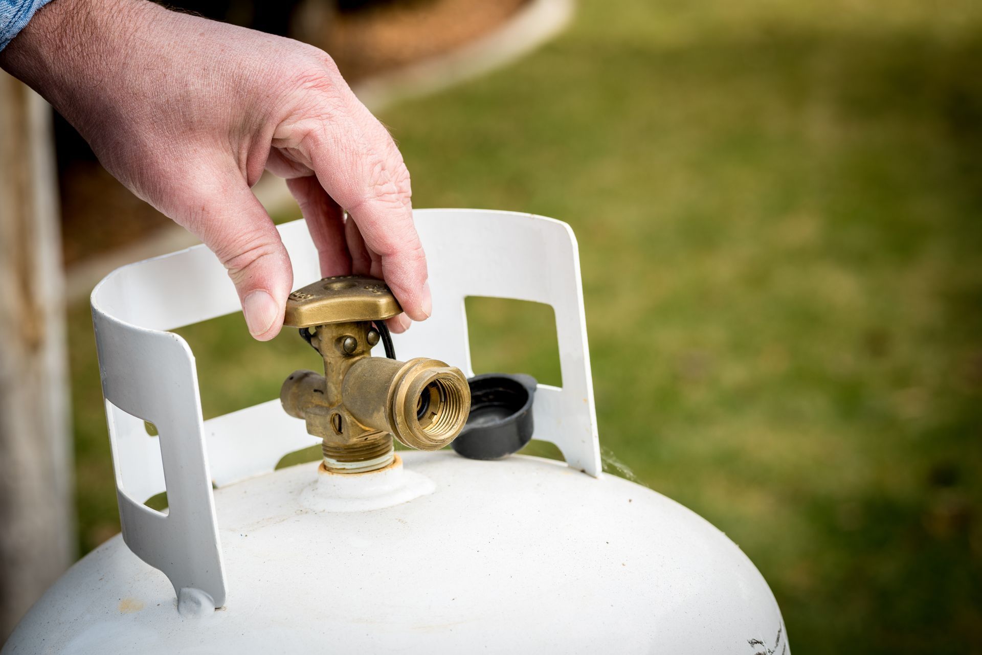 Hand connecting a brass propane tank valve to a white gas cylinder outdoors