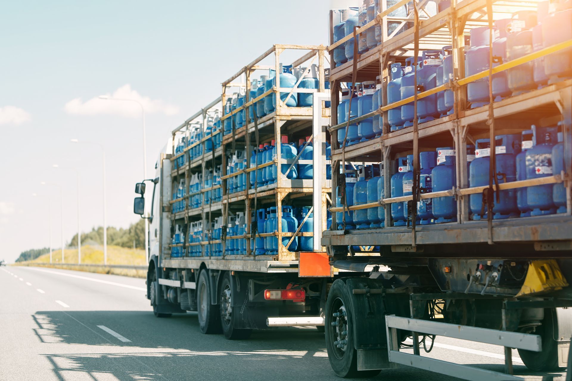 Two cargo trucks carrying blue crates on a highway under bright sunlight