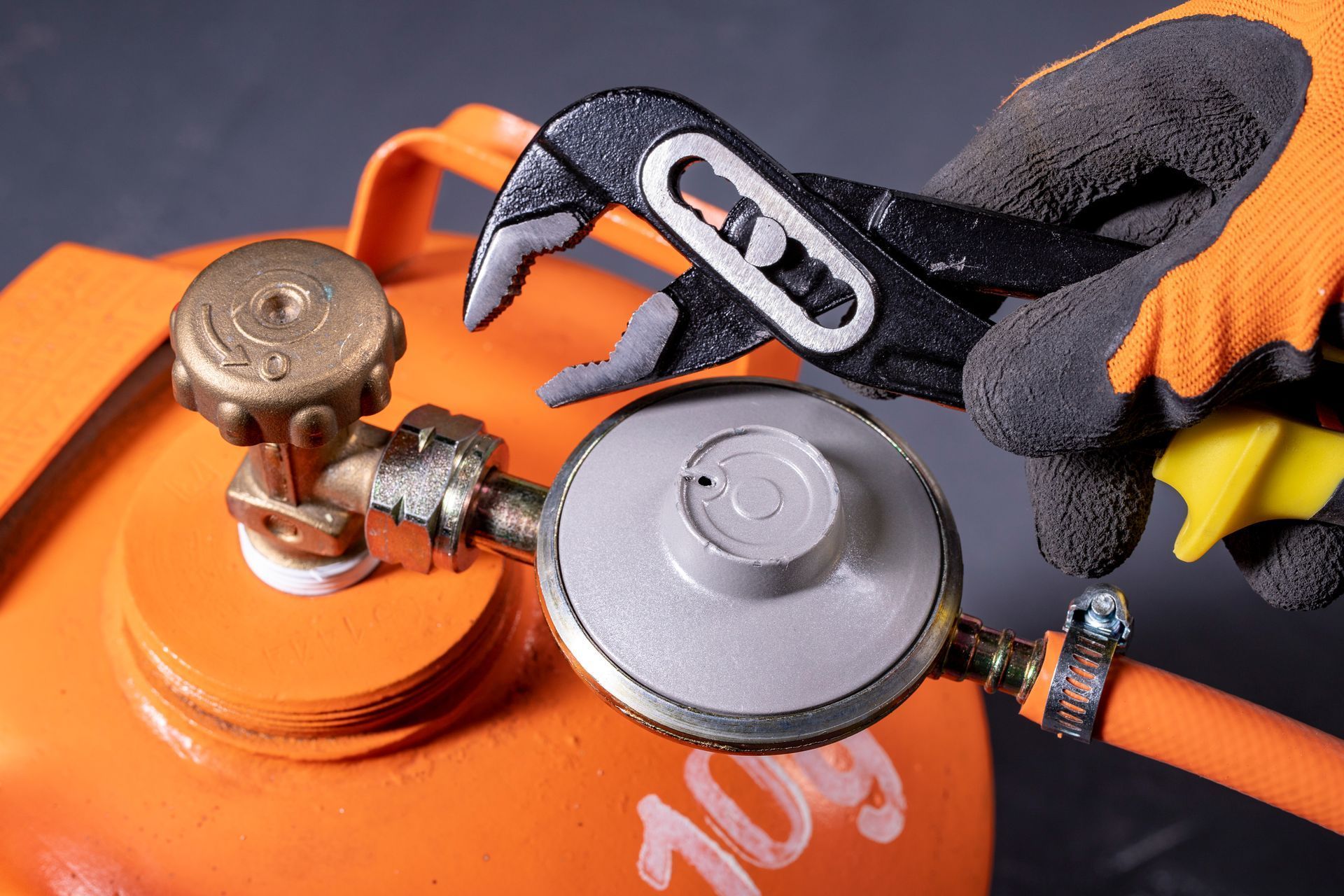 Gloved hands adjusting a gas cylinder valve with a wrench on an orange tank
