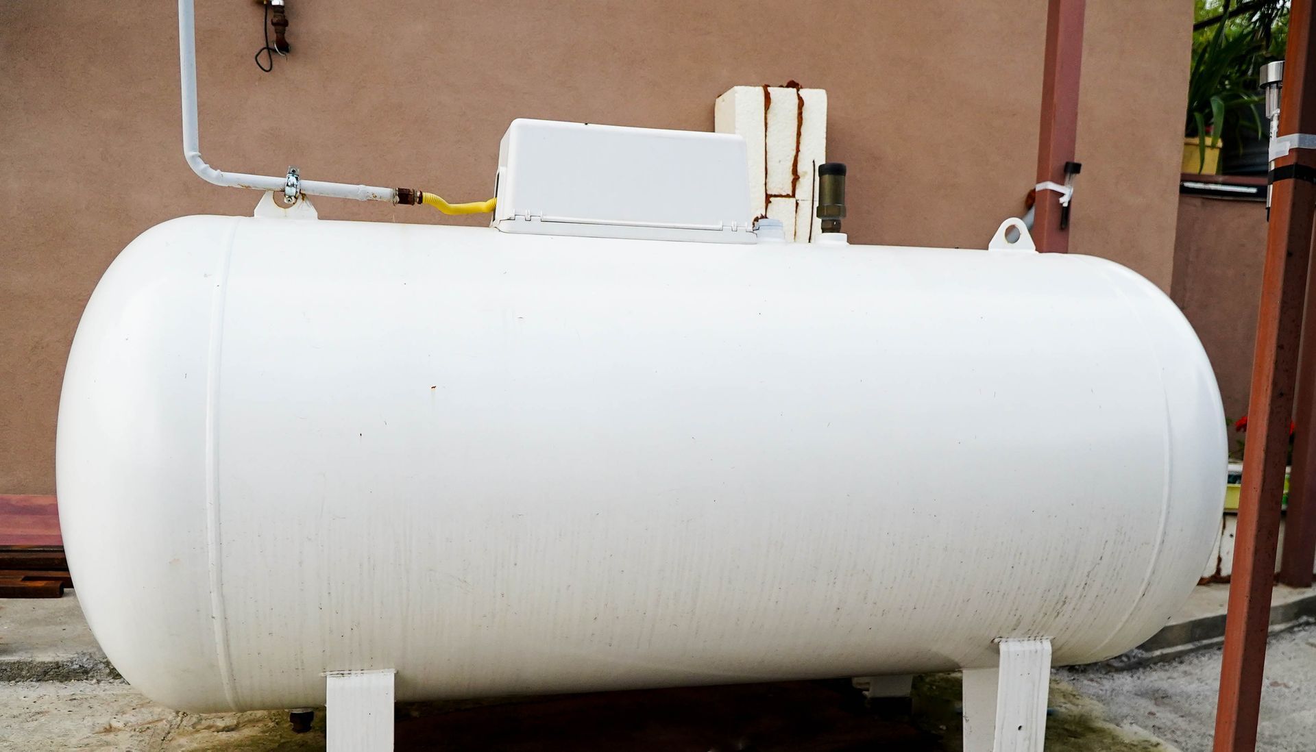 White horizontal propane tank on metal legs outdoors beside a building.