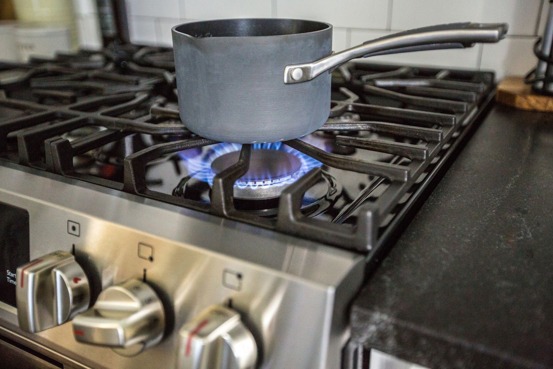 Small gray saucepan heating over a blue flame on a gas stove, with stainless steel knobs in front