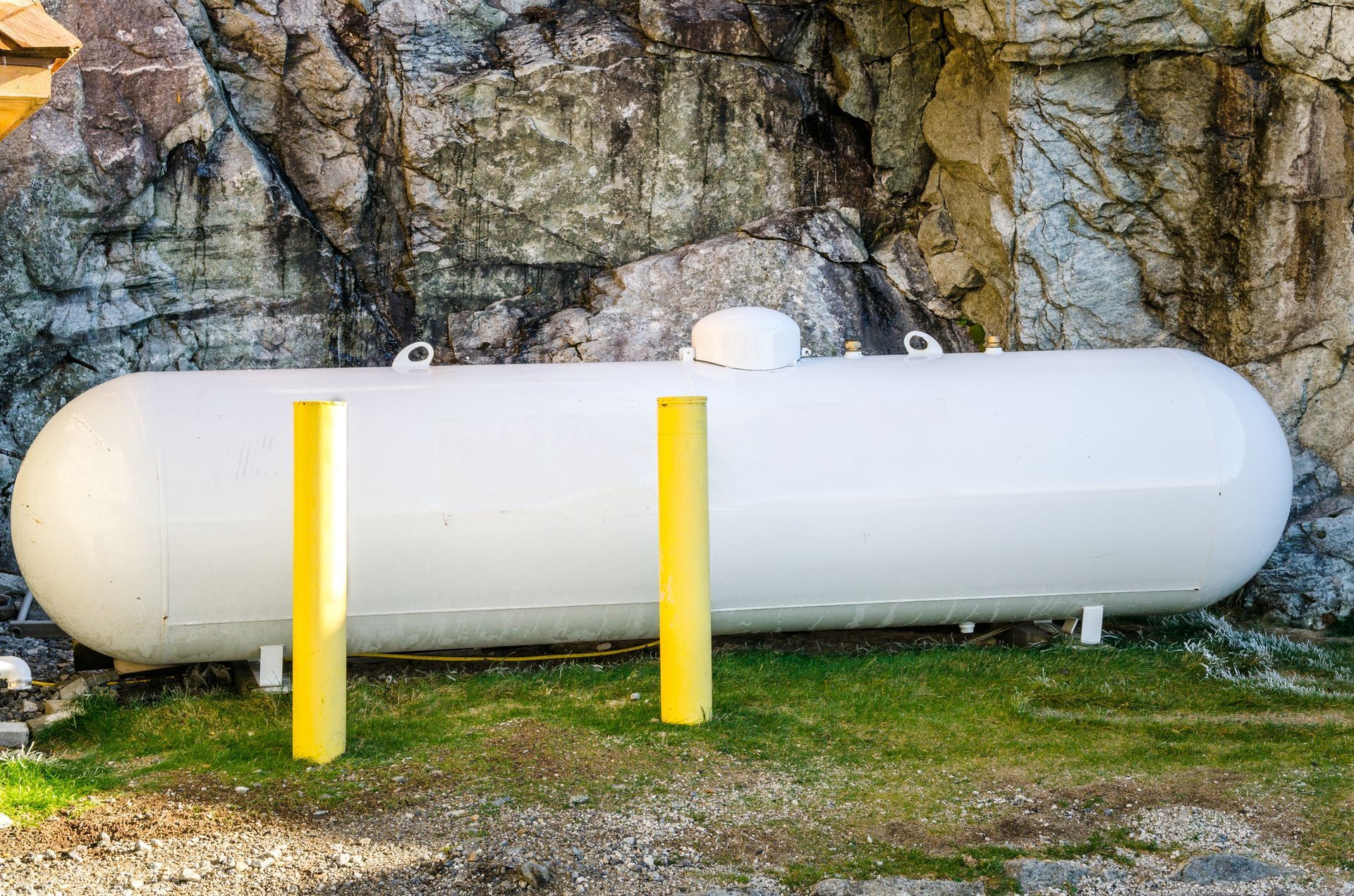 White cylindrical tank beside a rock wall, with two yellow posts in front